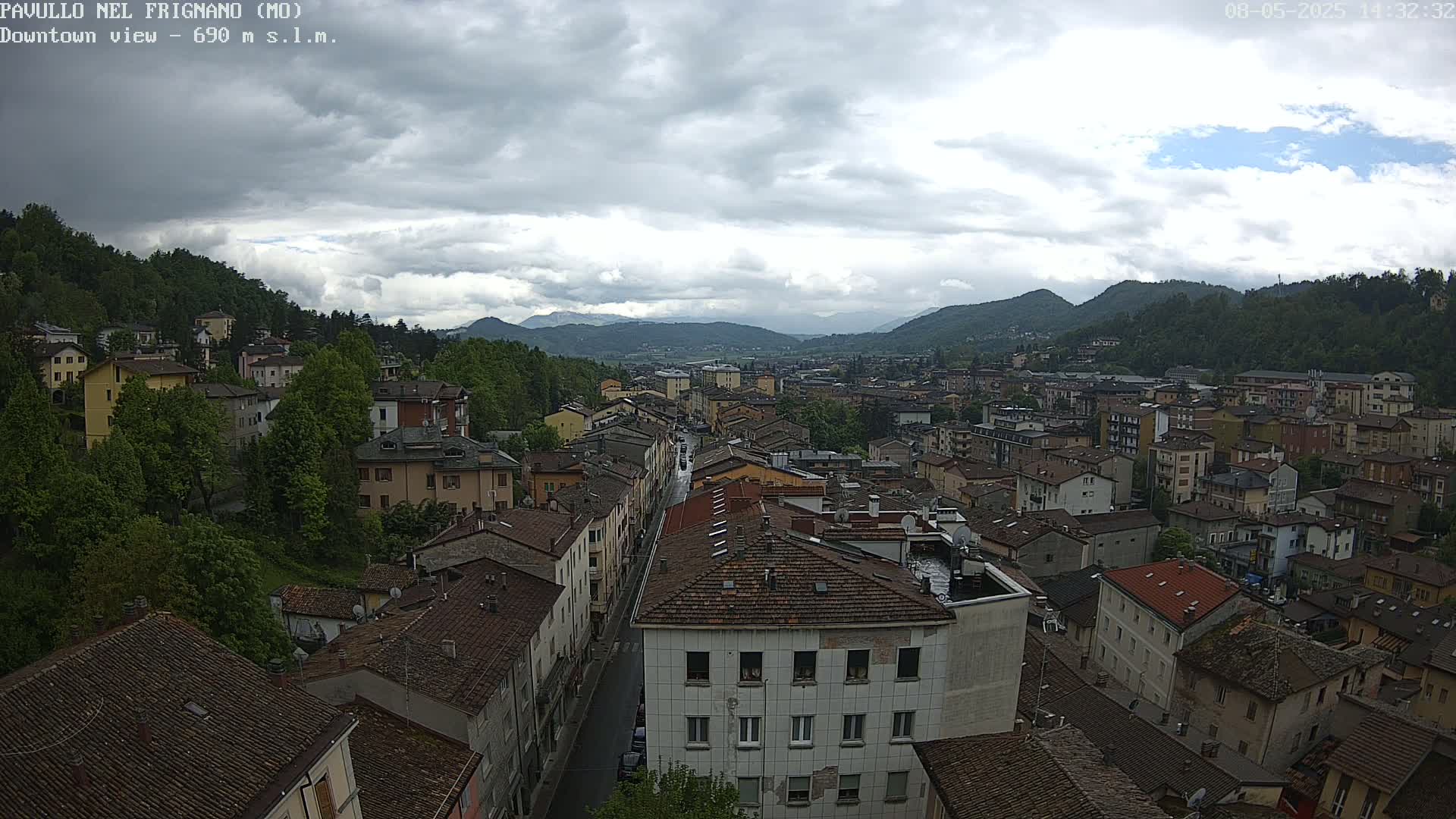 A view of a town nestled in a valley between green hills under a cloudy sky.