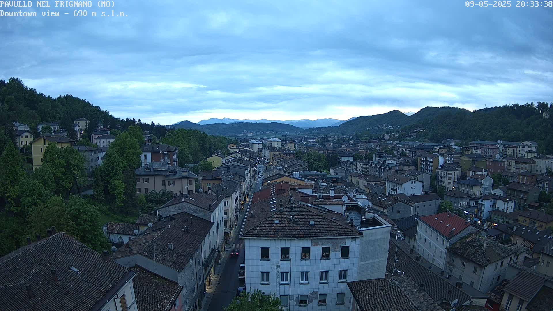 A sprawling town nestled in a valley under a twilight sky, surrounded by verdant hills and mountains.