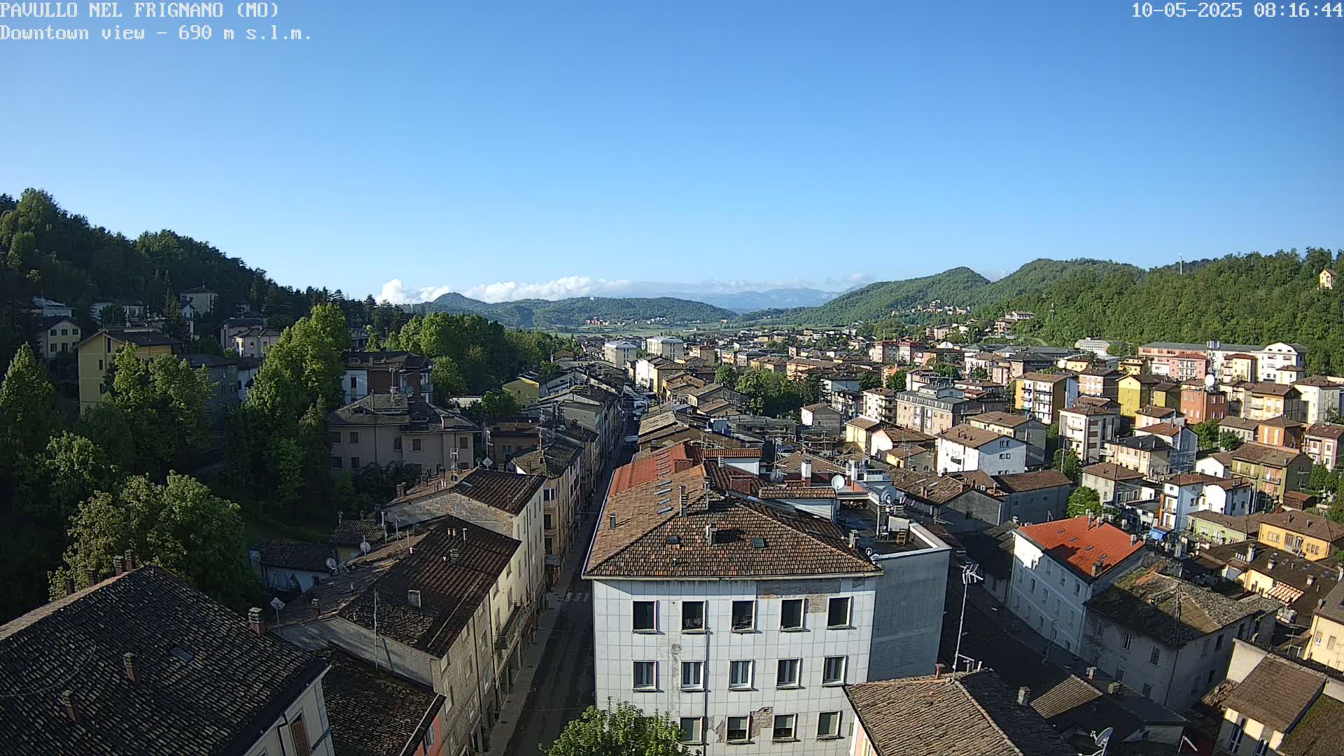 An aerial view of a town nestled in a valley under a clear blue sky, surrounded by green hills.