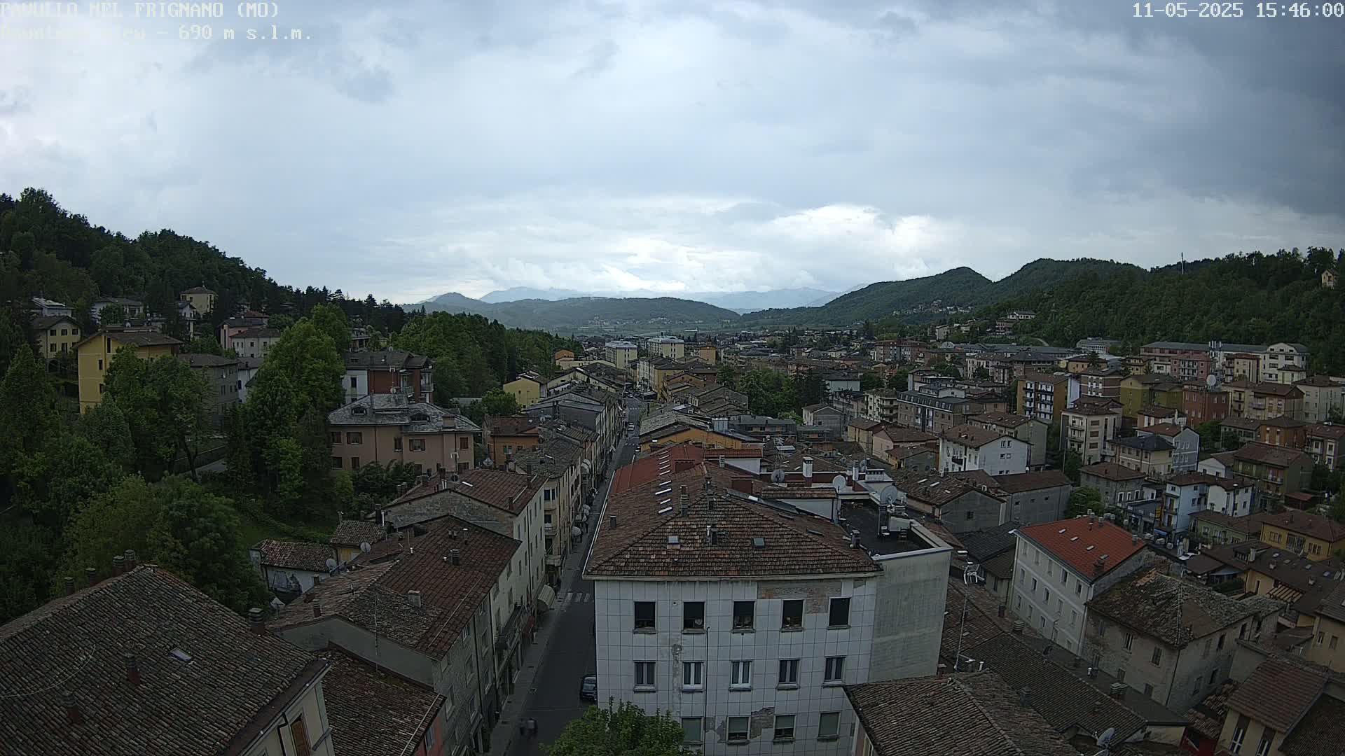 An aerial view of a town nestled in a valley between green hills under a cloudy sky.