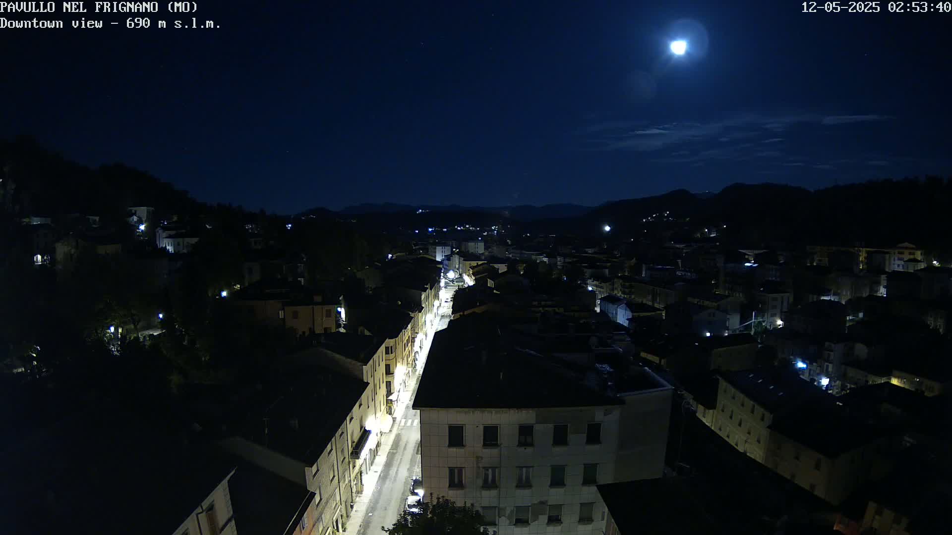 A moonlit night view shows a town nestled in hills, with a long street illuminated by lights.