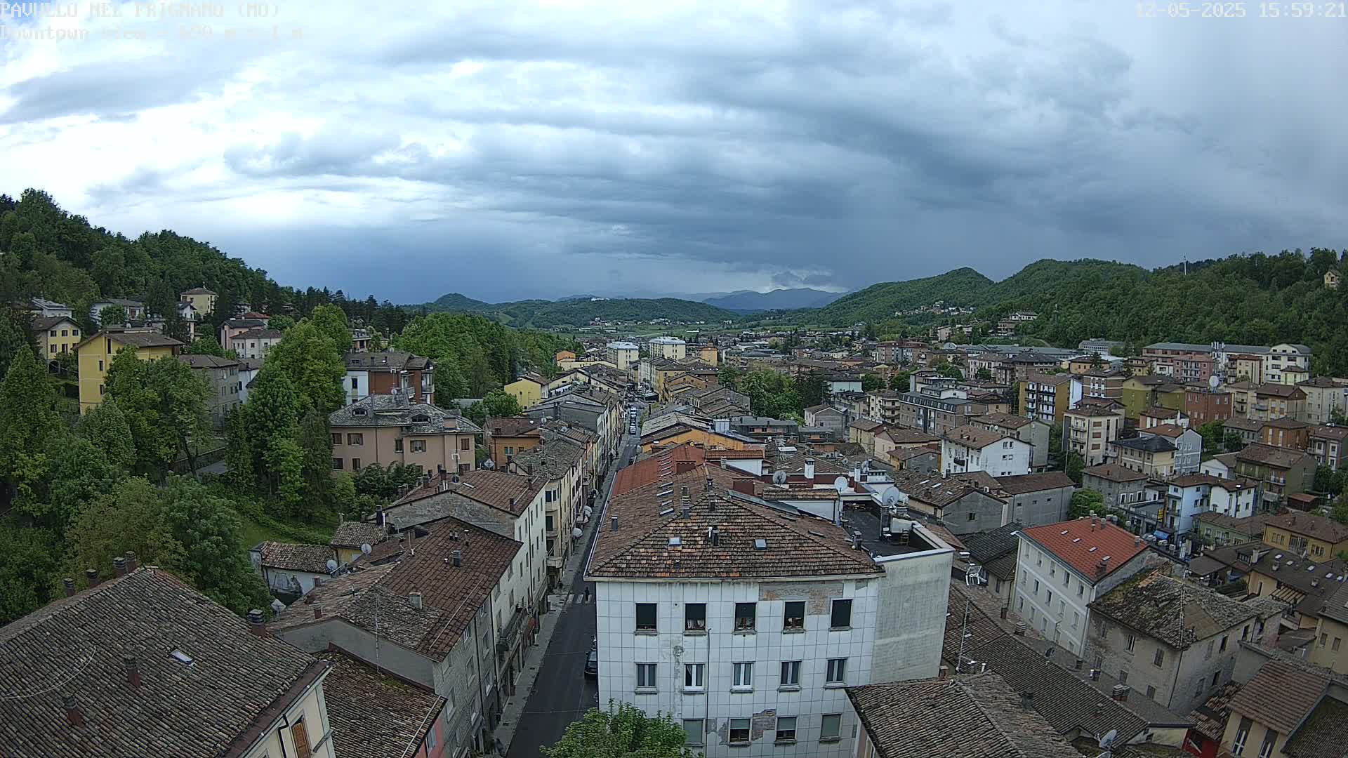 A sprawling town nestled in a valley under a cloudy sky, with green hills rising in the background.