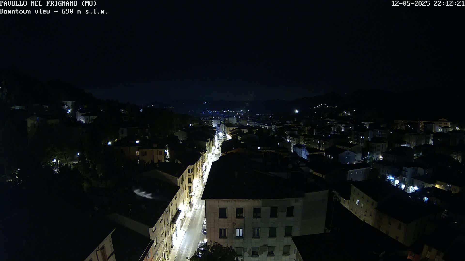 A nighttime, high-angle view of a town, illuminated by streetlights and building lights, nestled among dark hills under a clear night sky.