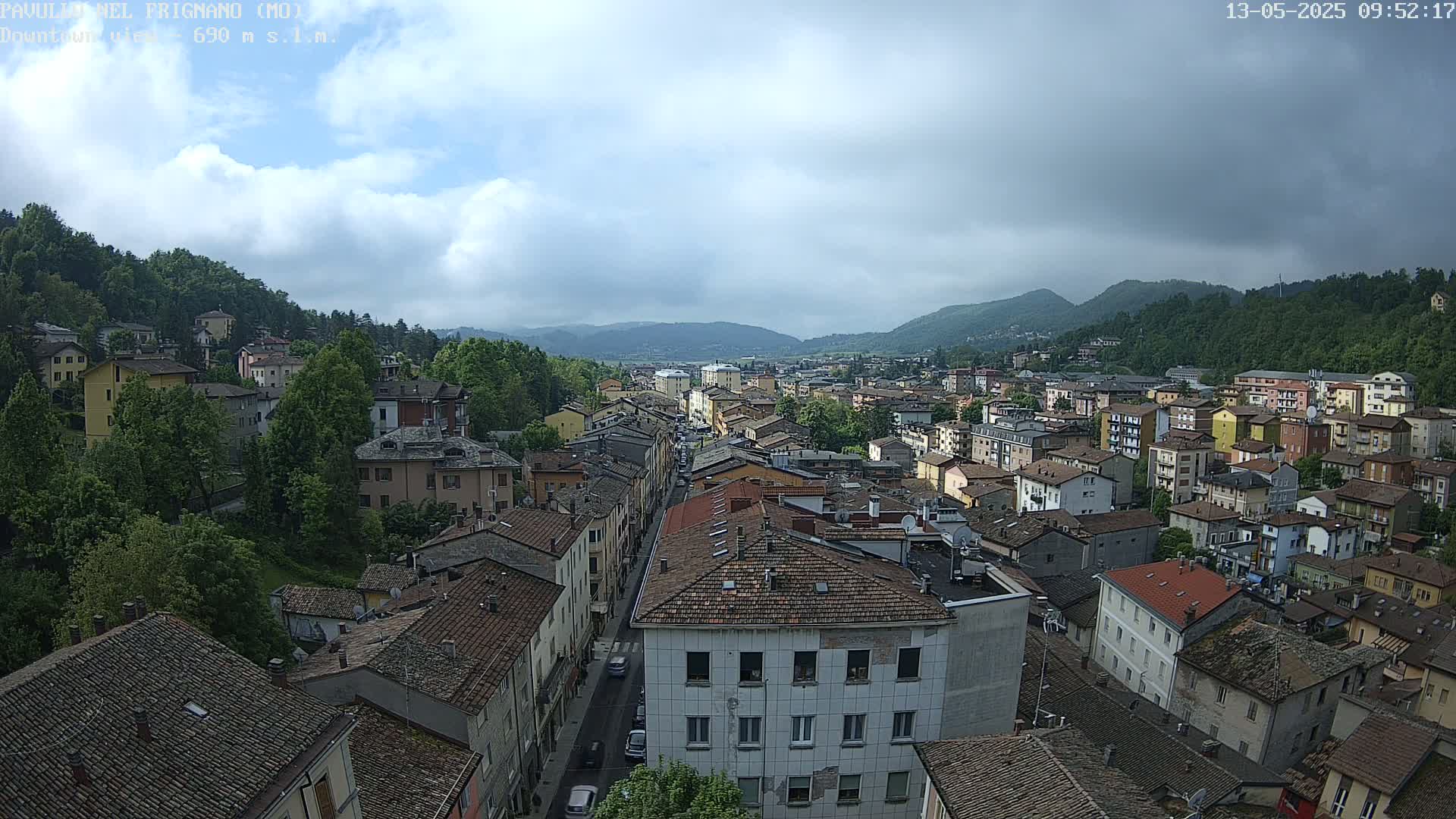 A sprawling town nestled in a valley between verdant hills under a partly cloudy sky.