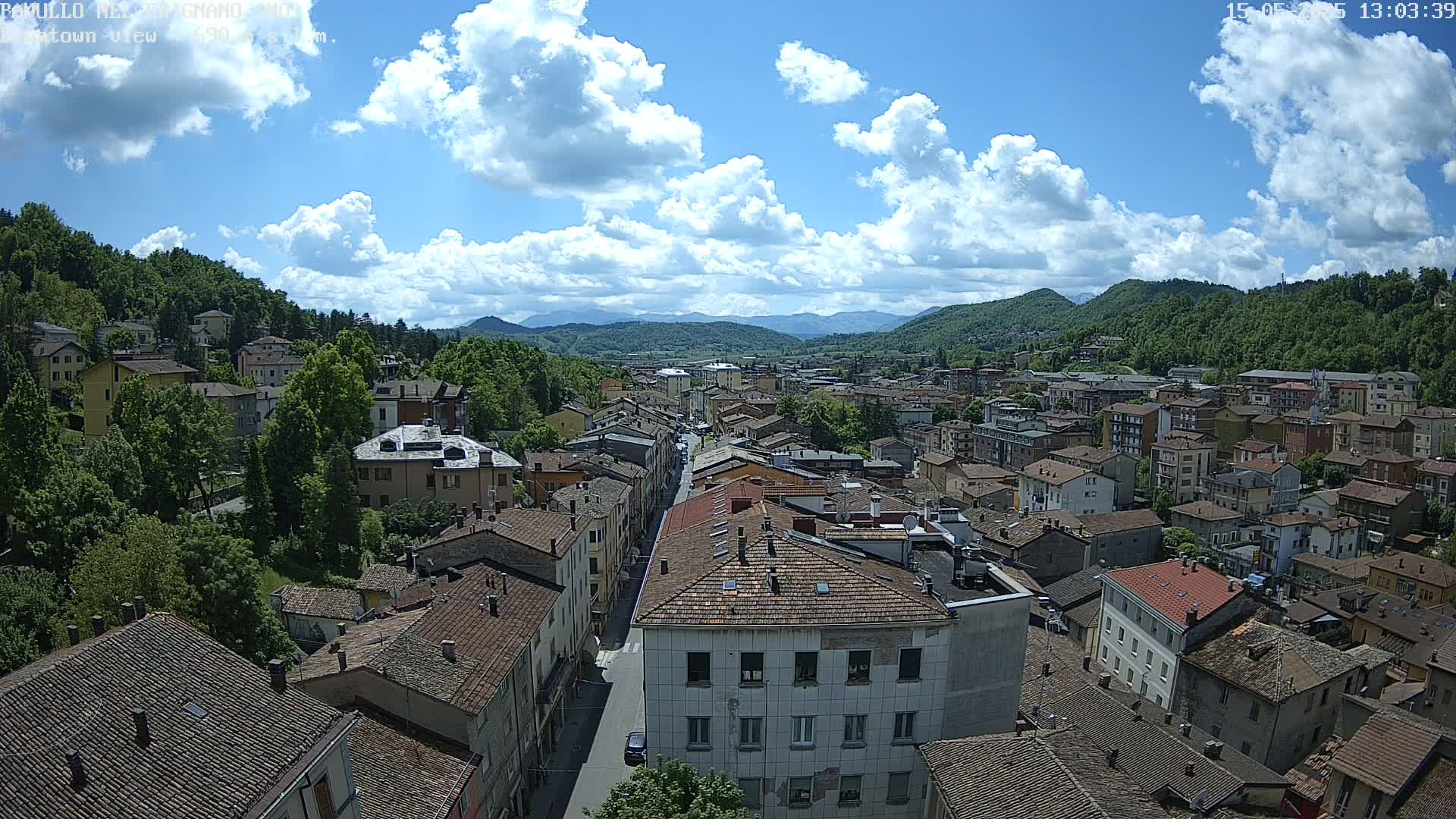 A partly sunny day reveals a sprawling town nestled in a valley surrounded by lush green hills and mountains.