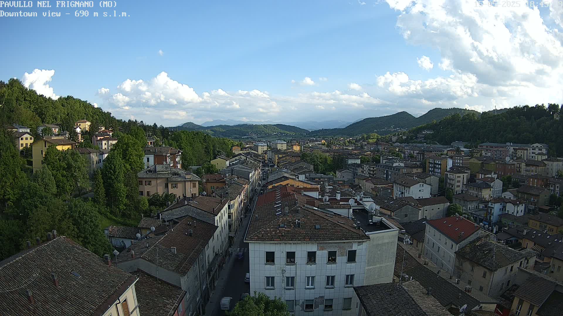 A partly cloudy sky overlooks a town nestled in a valley between green hills.