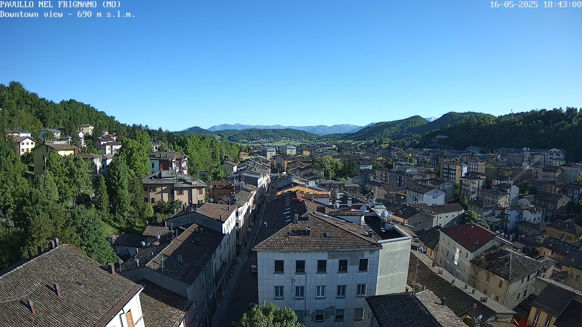 A sprawling town nestled in a valley between verdant hills under a clear blue sky.