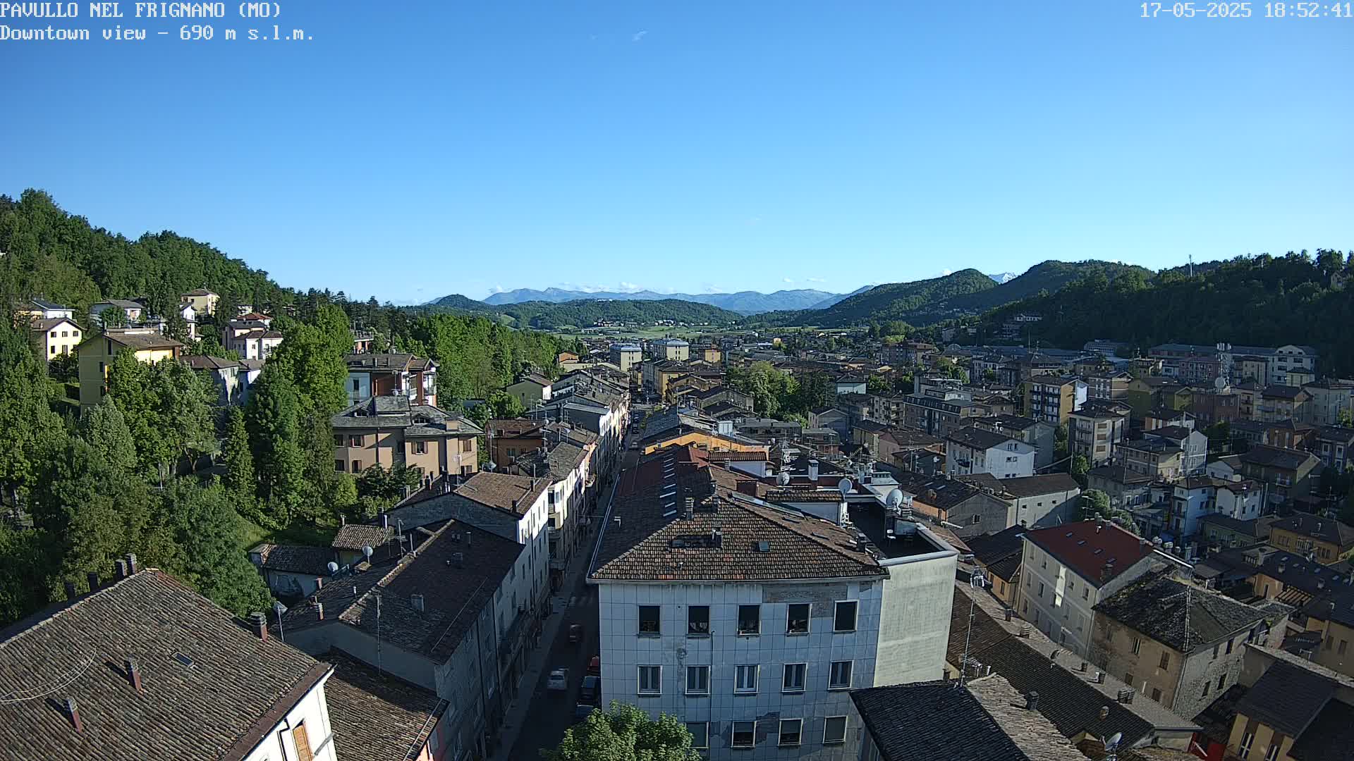 A clear, sunny day reveals a sprawling town nestled in a valley between mountains, with buildings tightly packed together.
