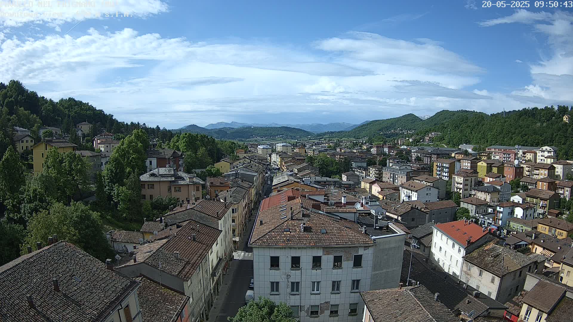 A partly cloudy day reveals a sprawling town nestled in a valley between verdant mountains.