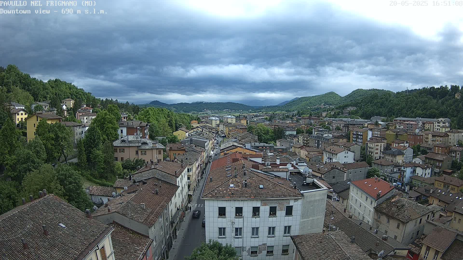 A sprawling town nestled in a valley under a cloudy sky, with mountains visible in the distance.