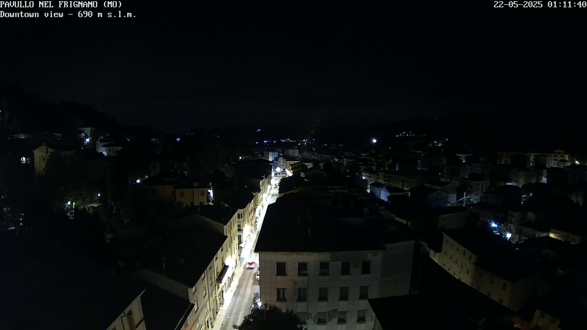 A nighttime, high-angle view of a town with a brightly lit street running through its center.