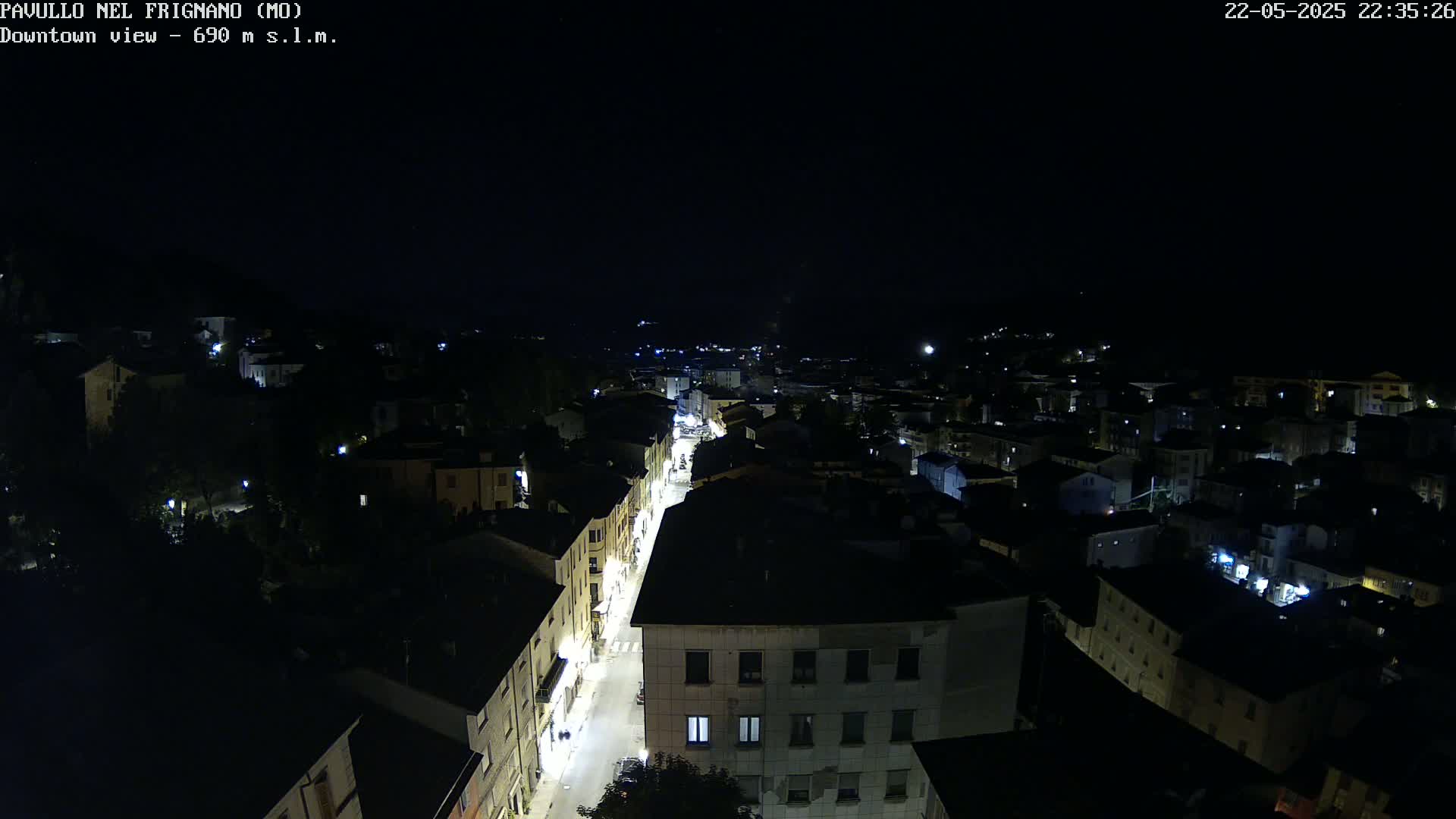 A nighttime, high-angle view shows a town's streetlights illuminating buildings and a road below.