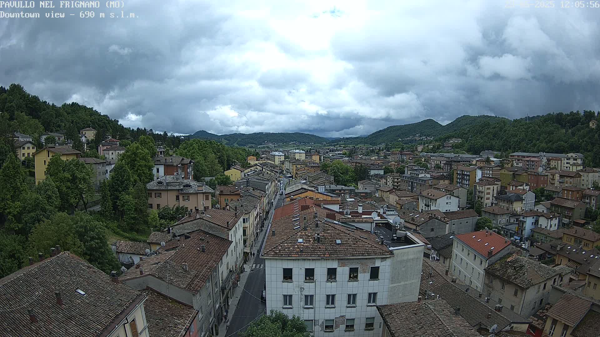 A sprawling town nestled in a valley between verdant hills under a cloudy sky.