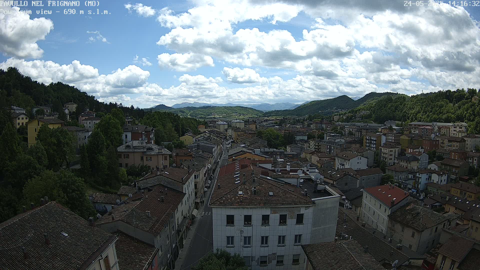 A partly cloudy sky overlooks a town nestled in a valley between green hills.