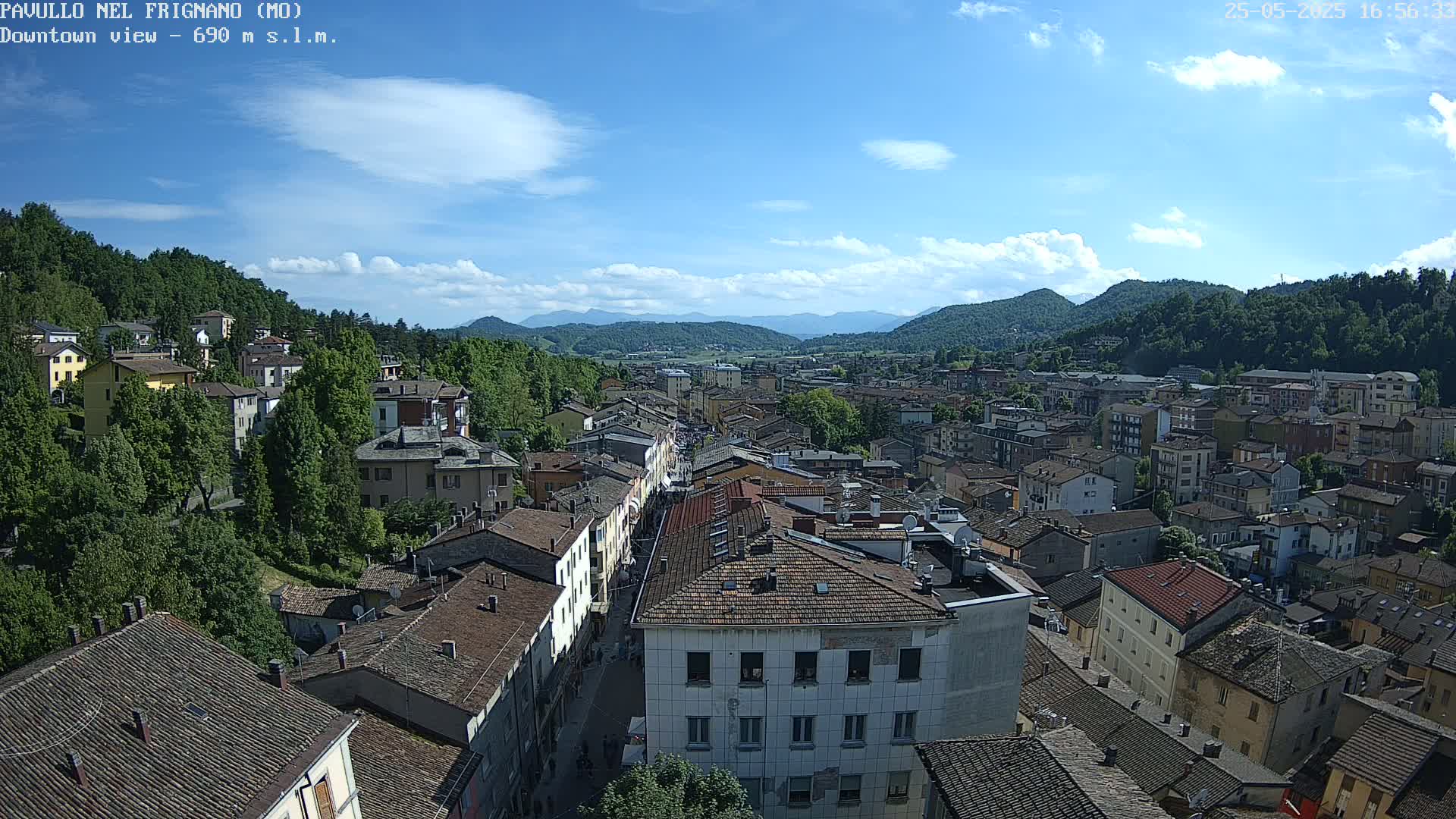 A high-angle view of a town nestled in a valley, under a mostly sunny sky with a few scattered clouds.