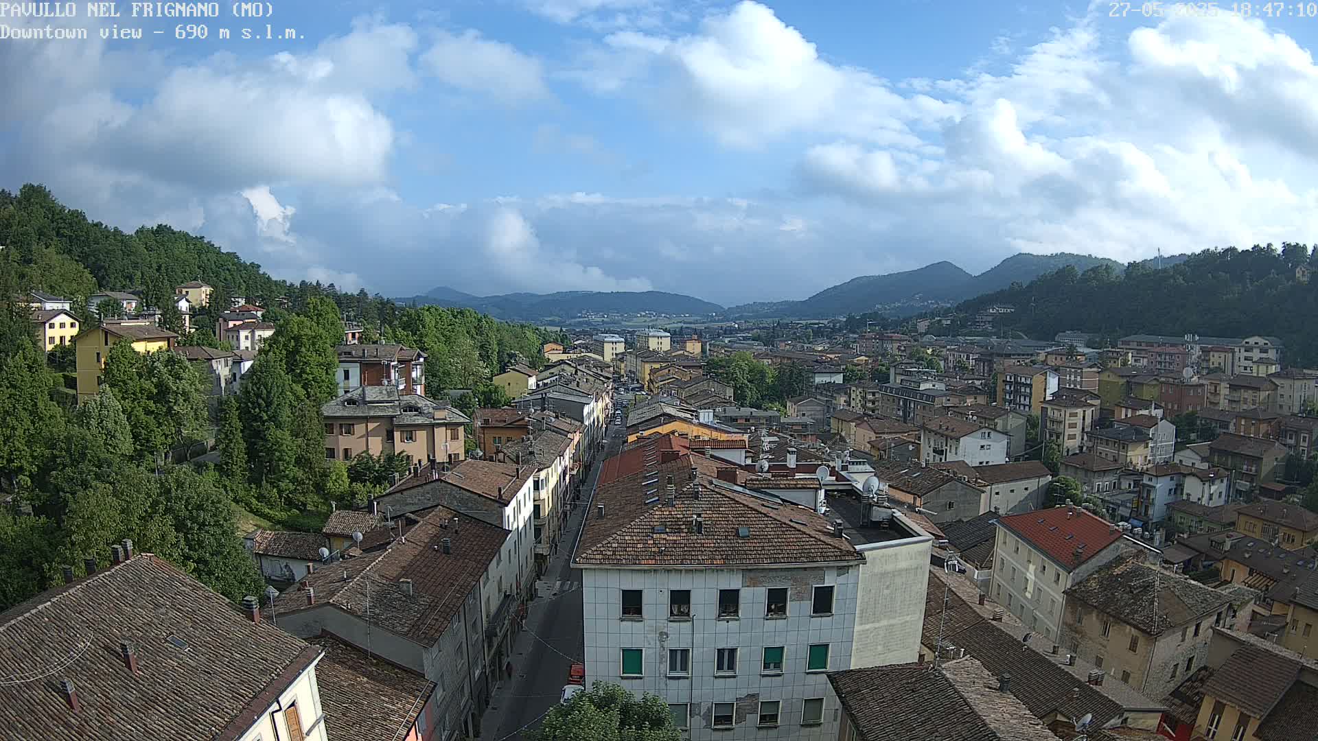 A partly cloudy day reveals a sprawling town nestled in a valley between verdant hills.