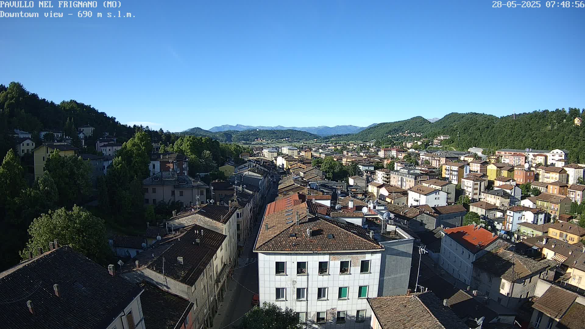 A sprawling town nestled in a valley between green hills under a clear blue sky.