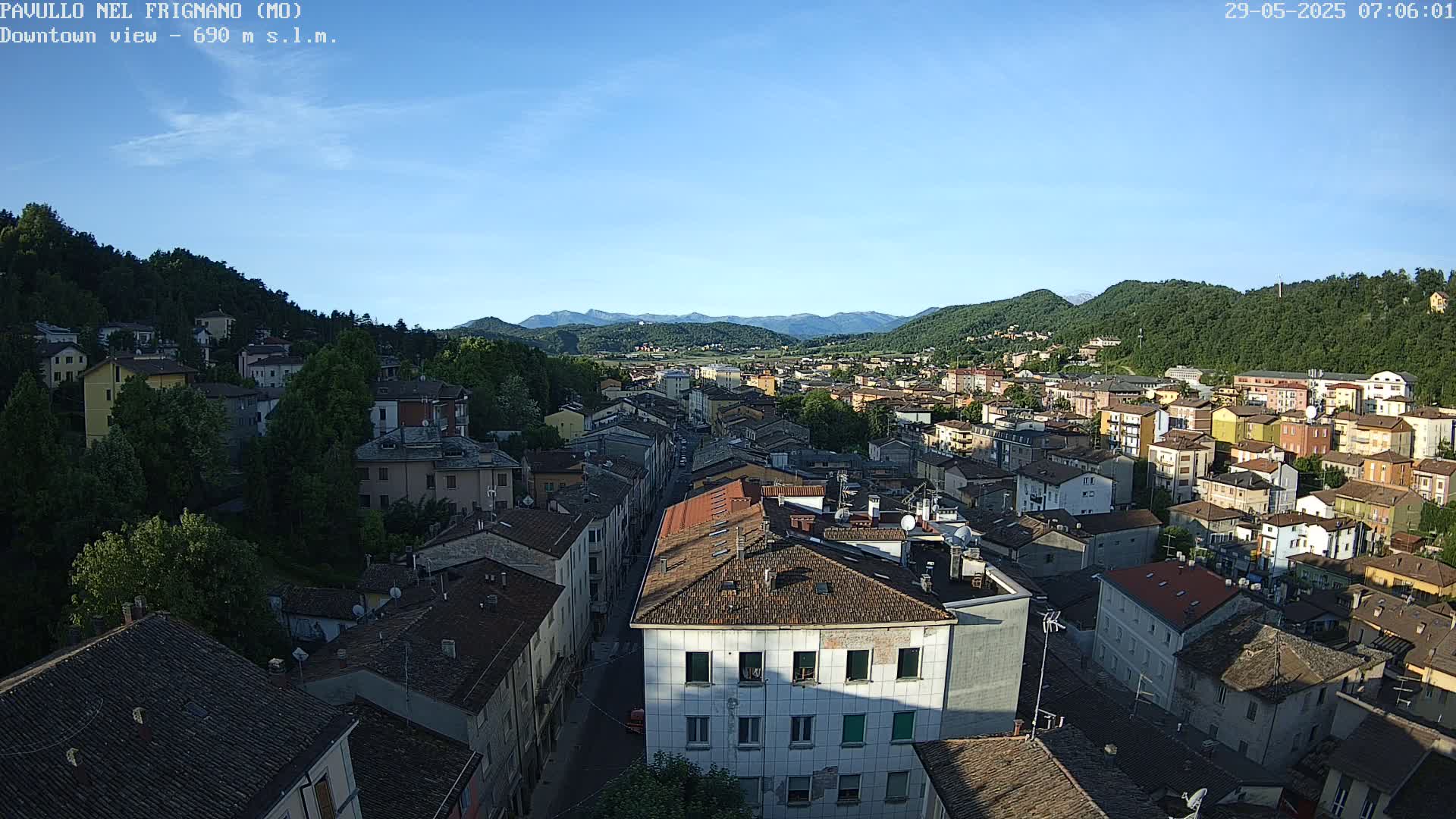 A sprawling town nestled in a valley between verdant hills under a clear blue sky.