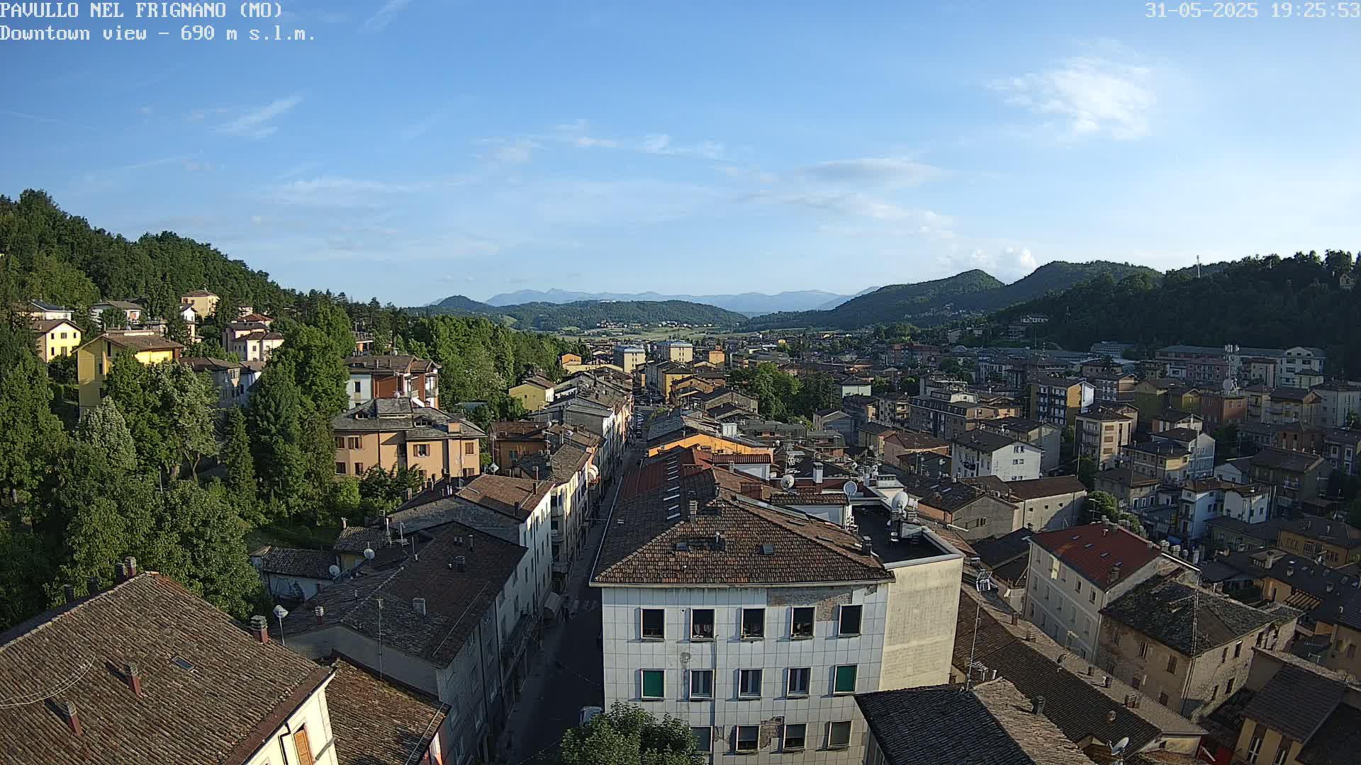An aerial view of a town nestled in a valley between mountains under a mostly clear, sunny sky.