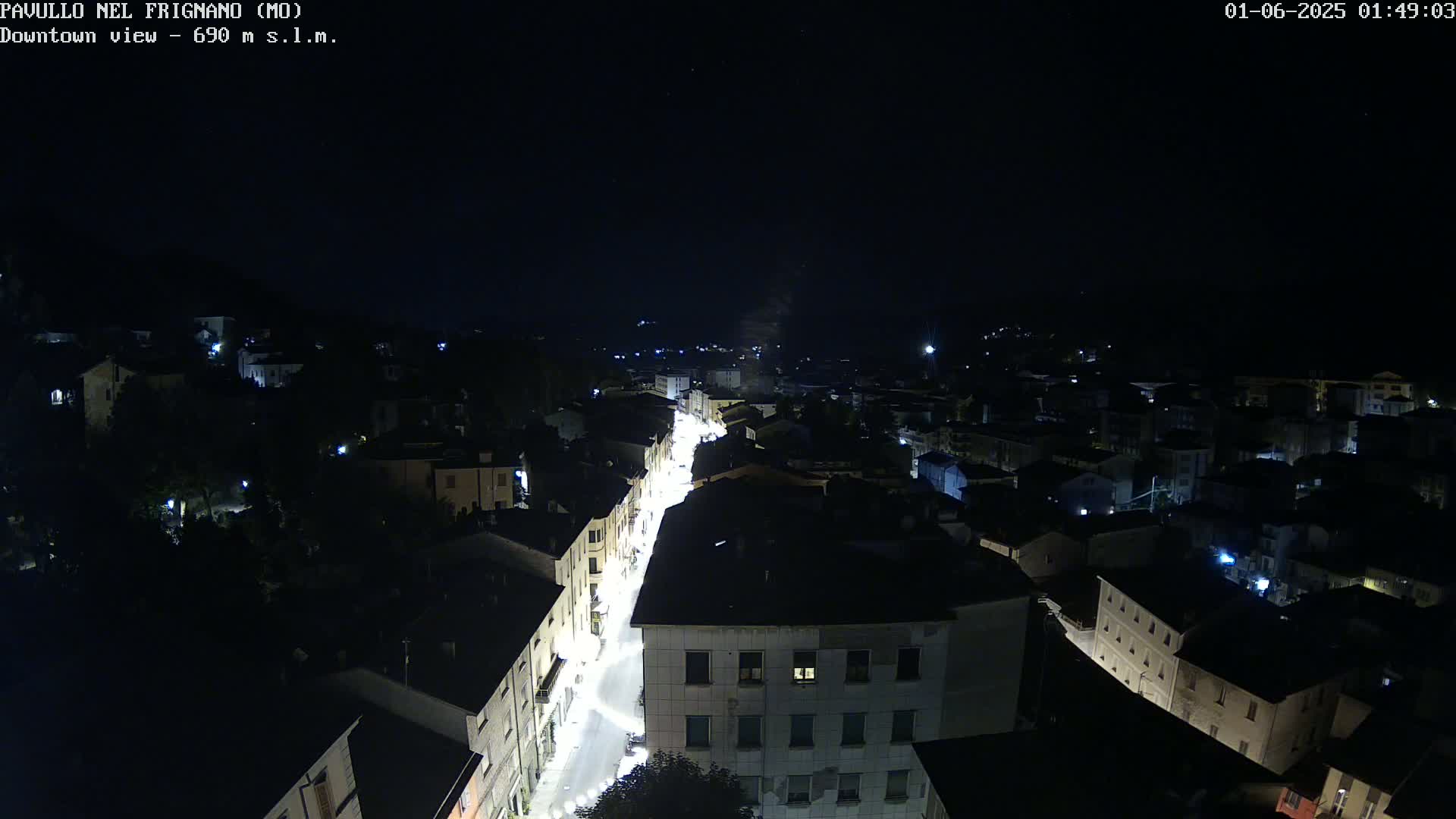 A nighttime, high-angle view of a town with a brightly lit street winding through it under a clear, starry sky.