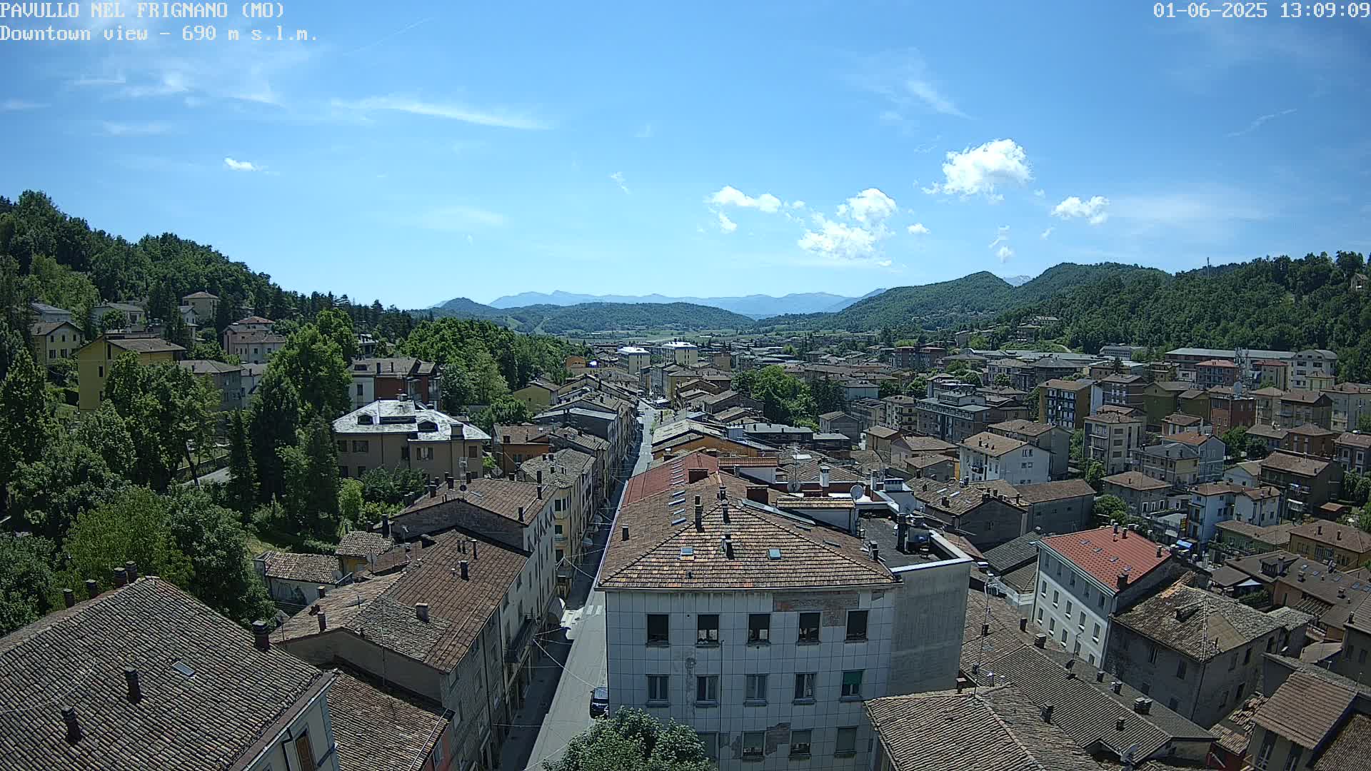 A small town nestled in a valley between mountains under a mostly sunny sky with a few scattered clouds.