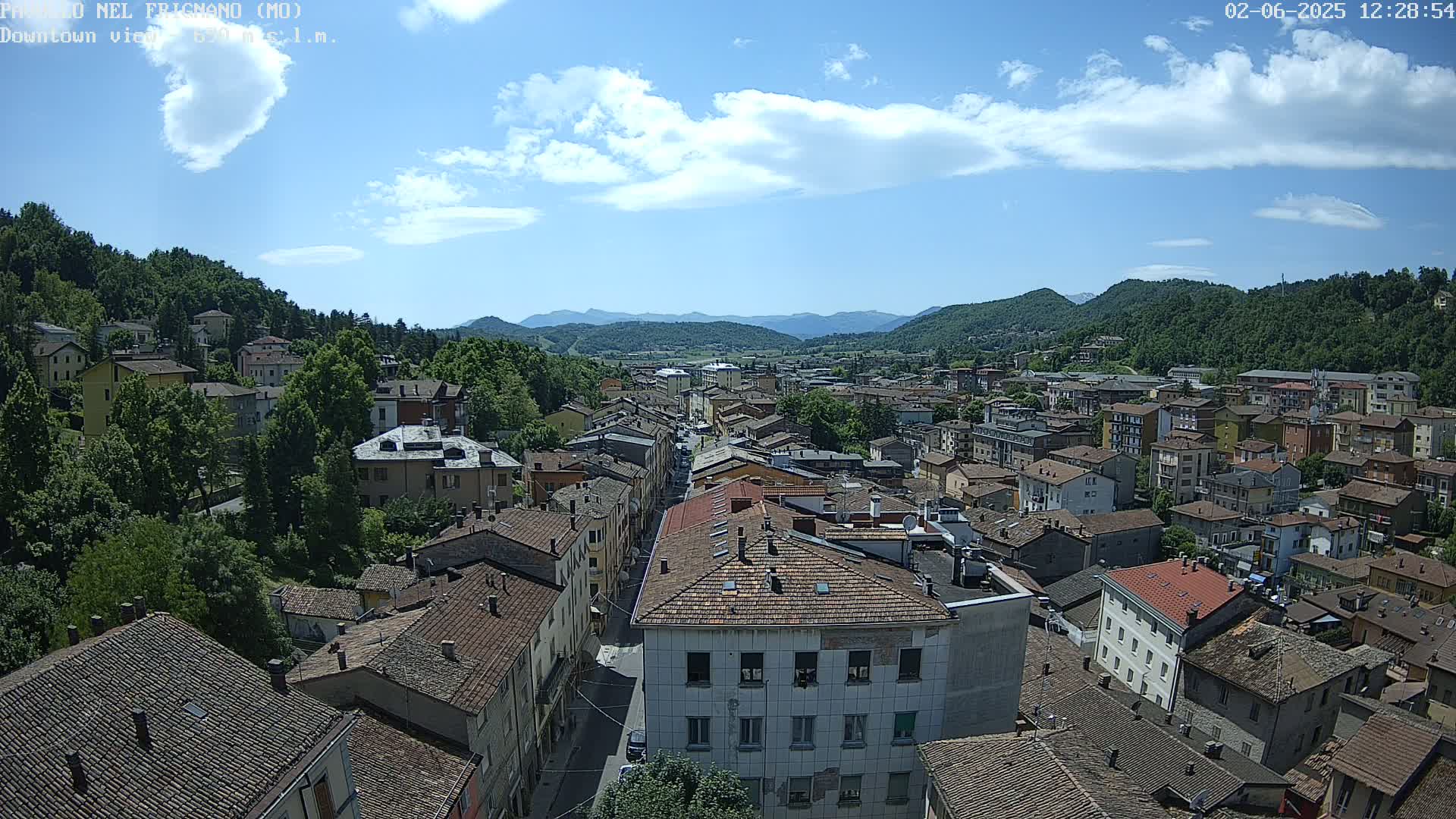 A sprawling town nestled in a valley between verdant hills under a partly cloudy sky.