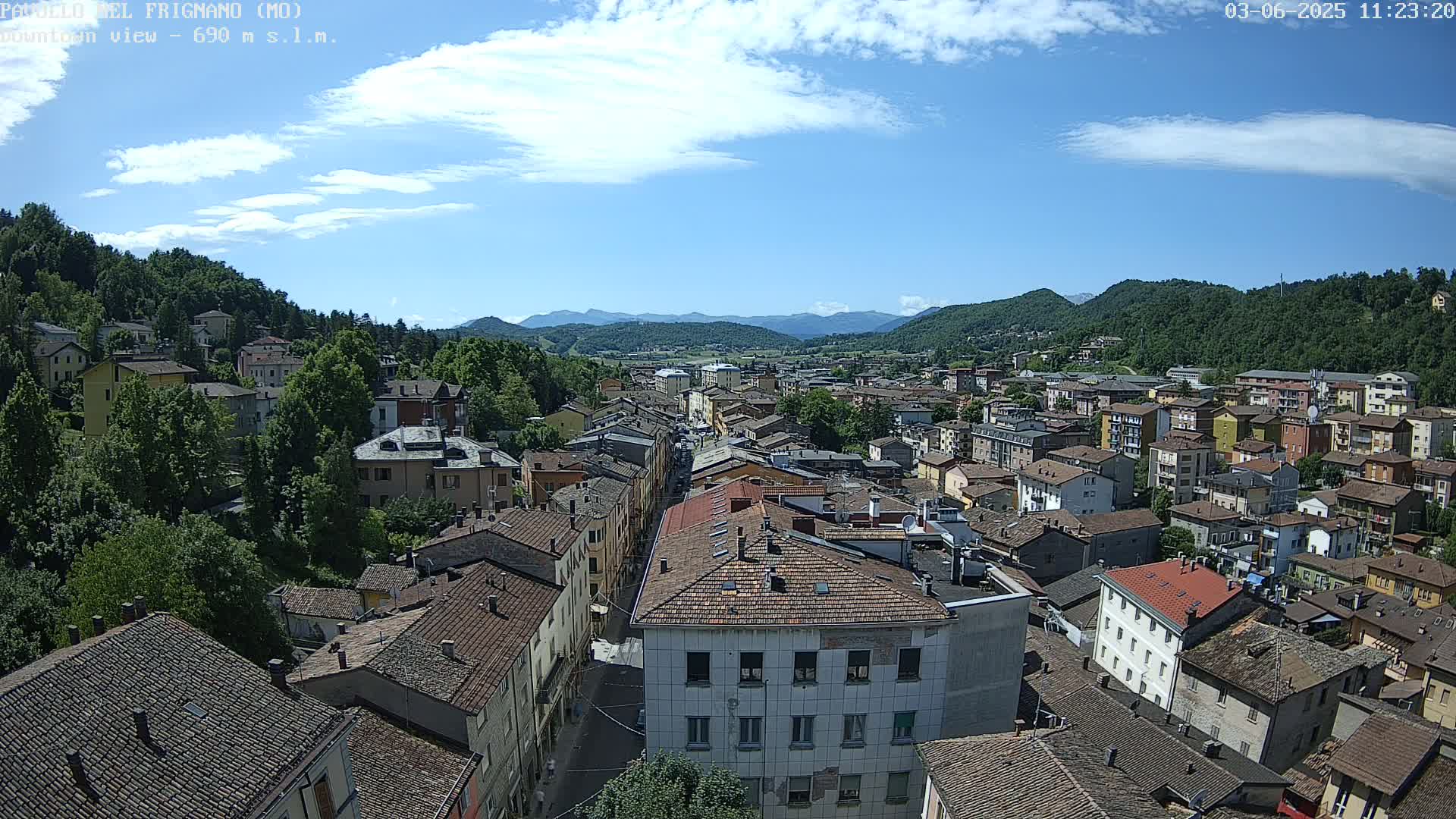 A sprawling town nestled in a valley between lush green hills under a mostly sunny sky with a few scattered clouds.