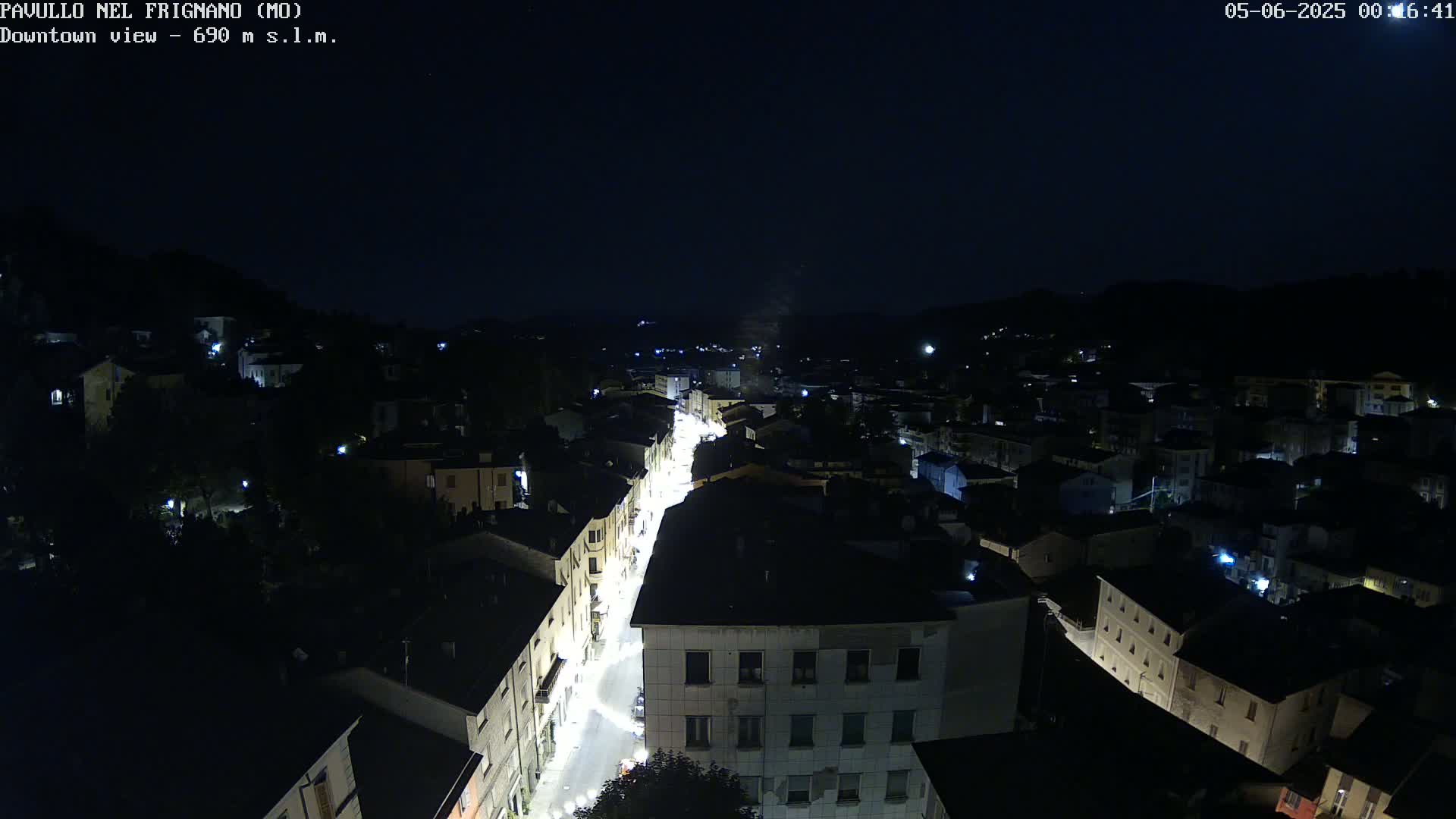 A nighttime, high-angle view of a town with a brightly lit street running through its center.