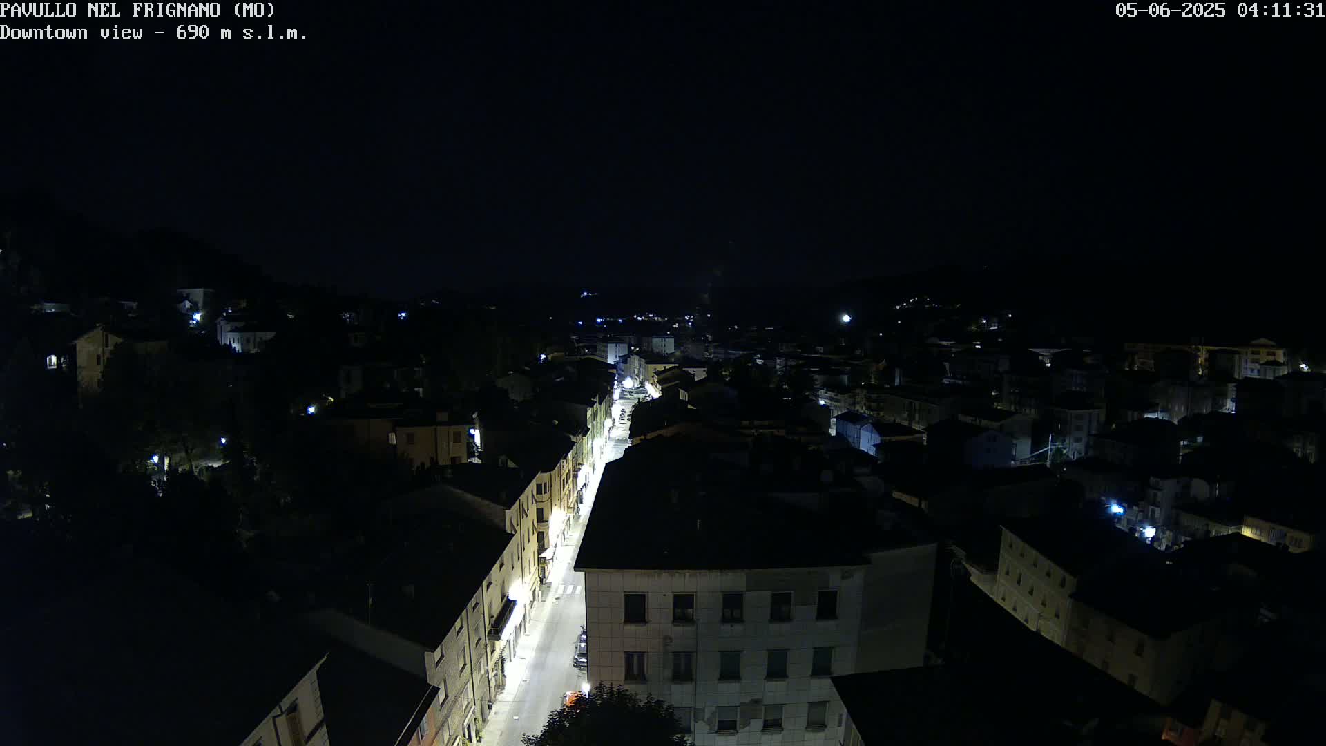An aerial nighttime view shows a town with a brightly lit street running through its center under a clear, dark sky.