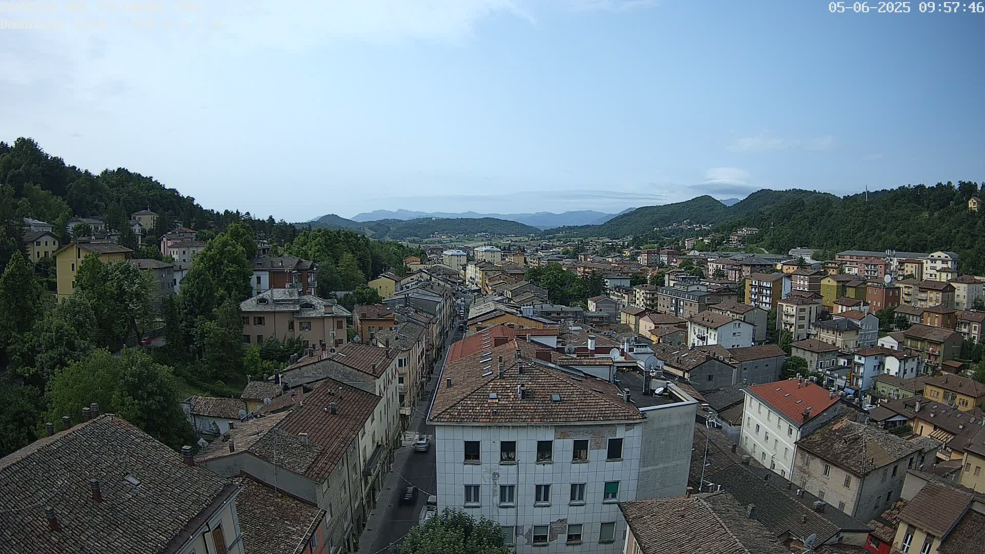 A sprawling town nestled in a valley between verdant hills under a mostly clear sky.