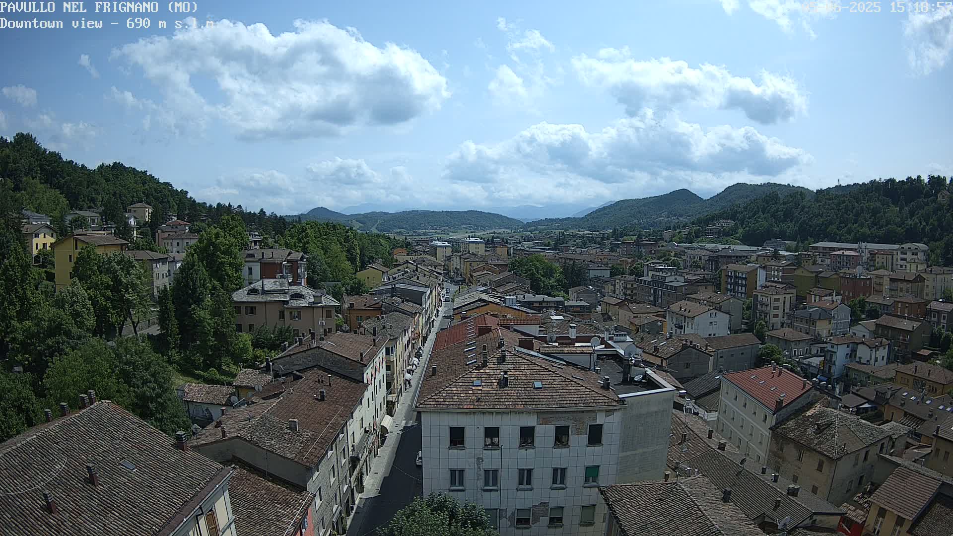 A partly sunny day reveals a town nestled in a valley between hills, with a long street running through its center.