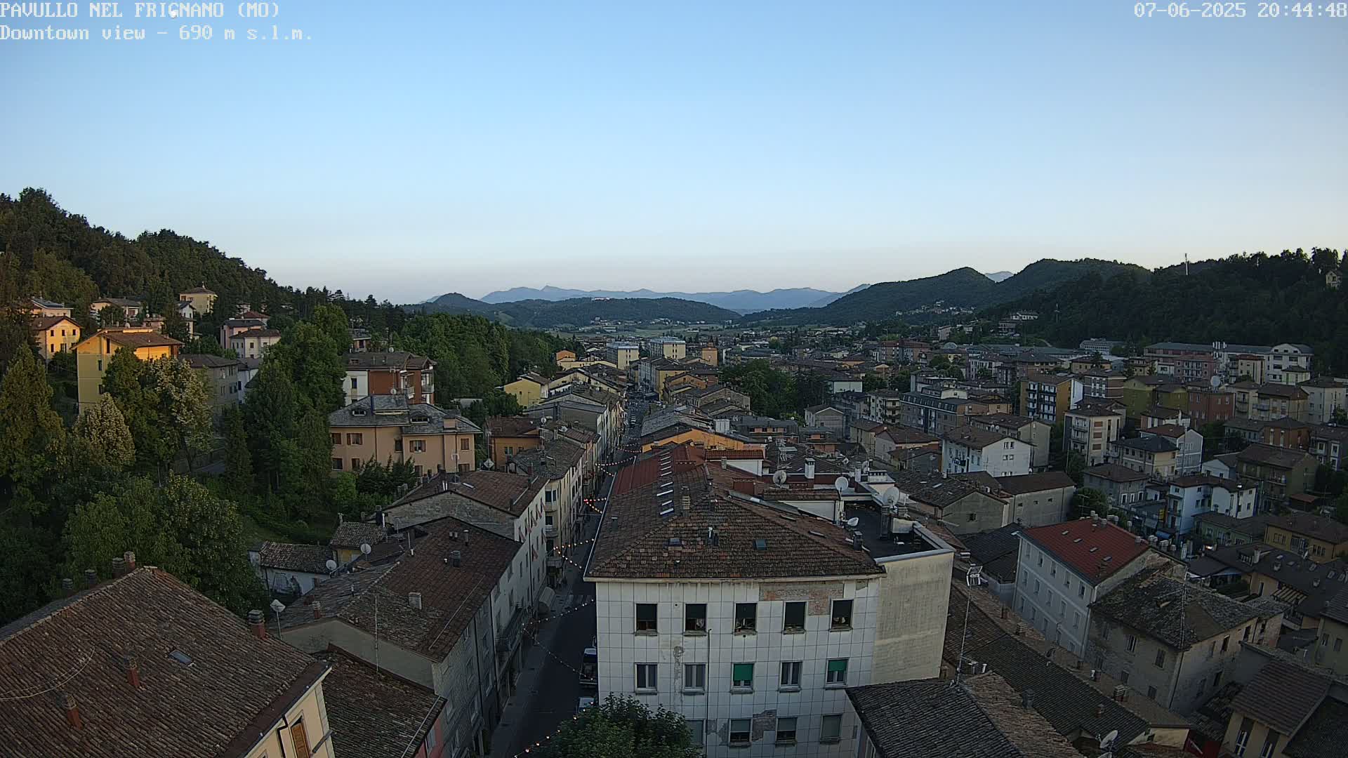 An elevated view of a town nestled in a valley, under a clear twilight sky, with distant mountains visible in the background.
