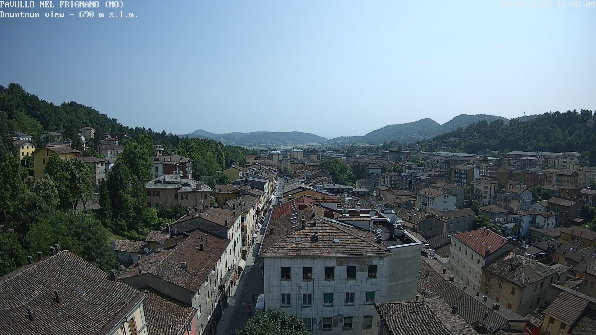 An elevated view of a town nestled in a valley on a clear, sunny day, surrounded by verdant hills.