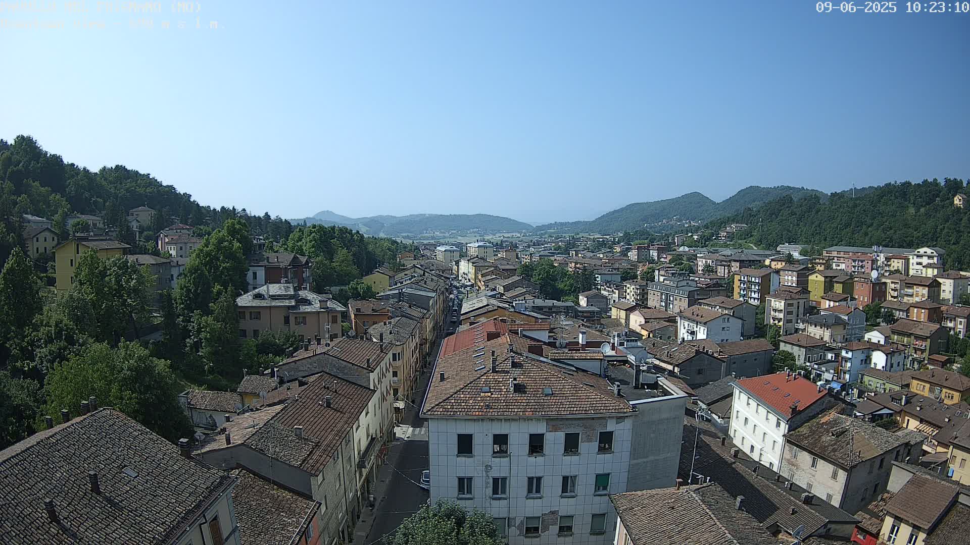 A sprawling town nestled in a valley between verdant hills under a clear, sunny sky.