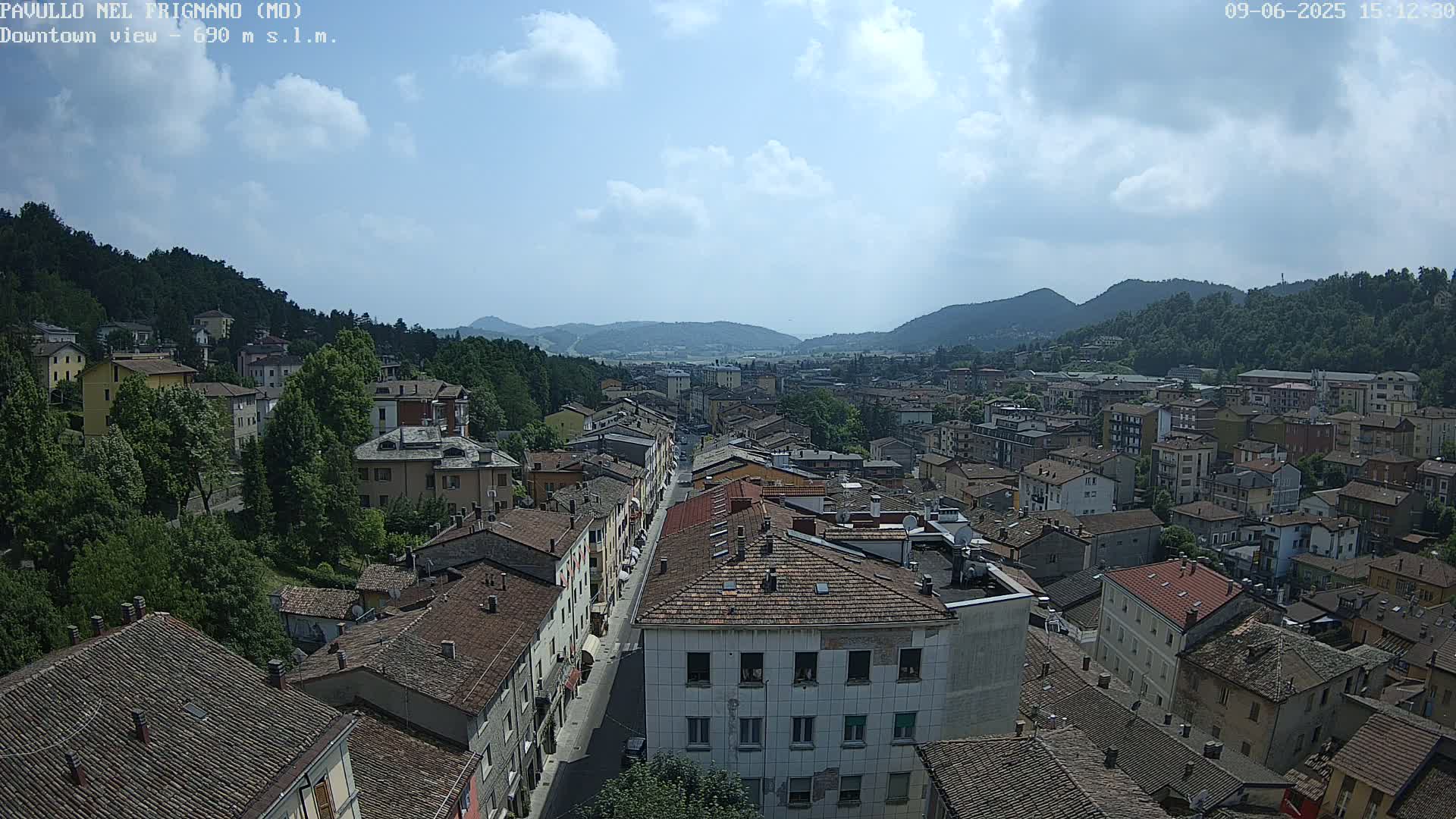 A partly sunny day reveals a sprawling town nestled in a valley surrounded by lush green hills.