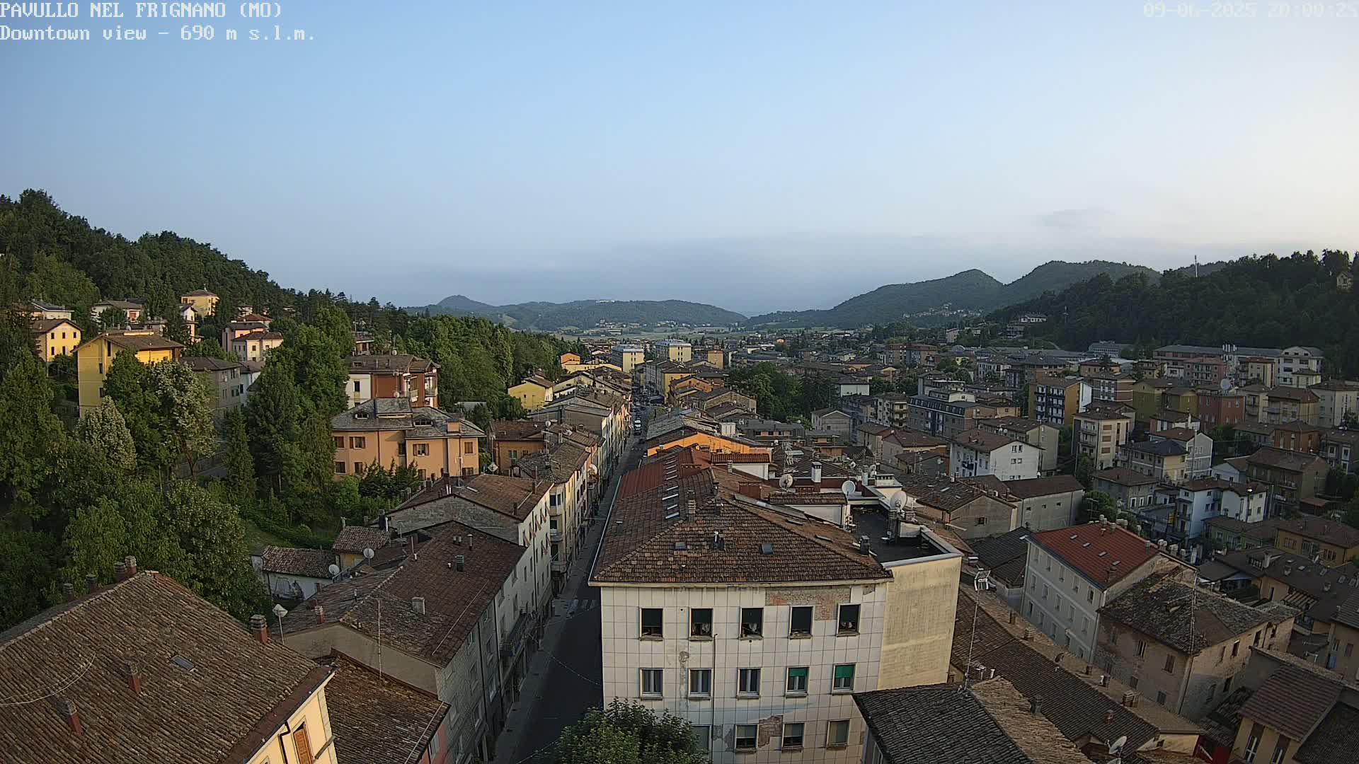 A sprawling town nestled in a valley between verdant hills under a clear, pale blue sky.