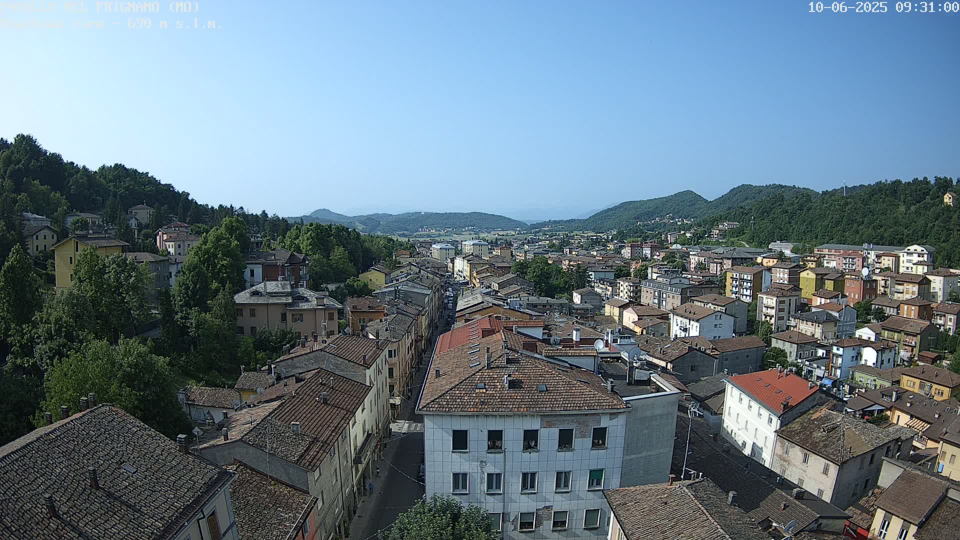 A sprawling town nestled in a valley between green hills under a clear blue sky.
