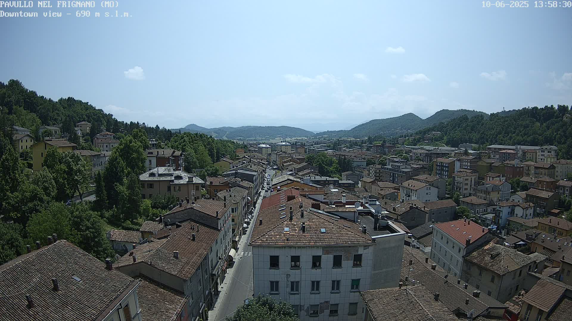 A sprawling town nestled in a valley under a mostly clear, sunny sky, with mountains visible in the distance.