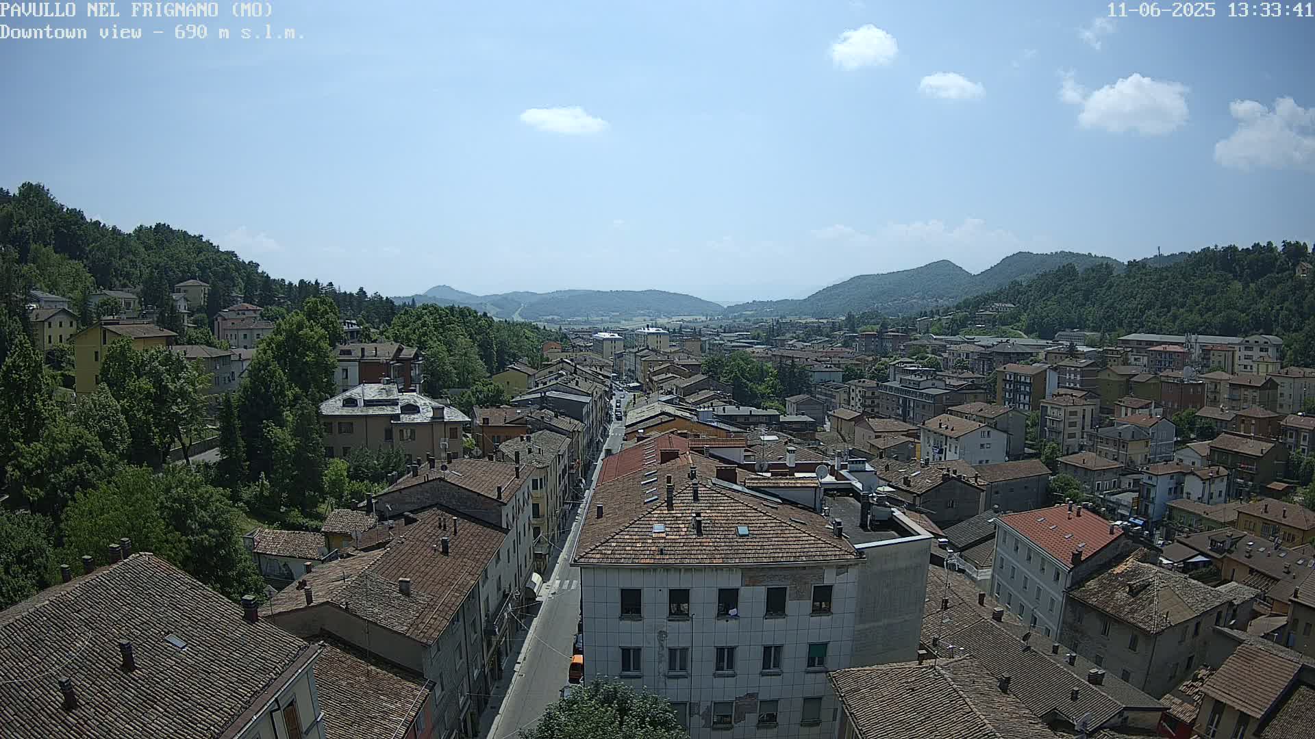 A sprawling town nestled in a valley between green hills under a mostly sunny sky with a few scattered clouds.