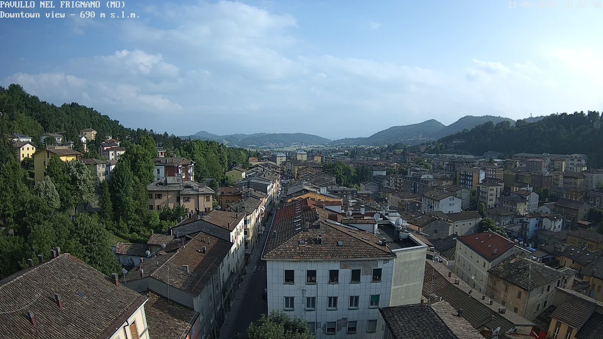A sprawling town nestled in a valley between green hills under a mostly clear sky.