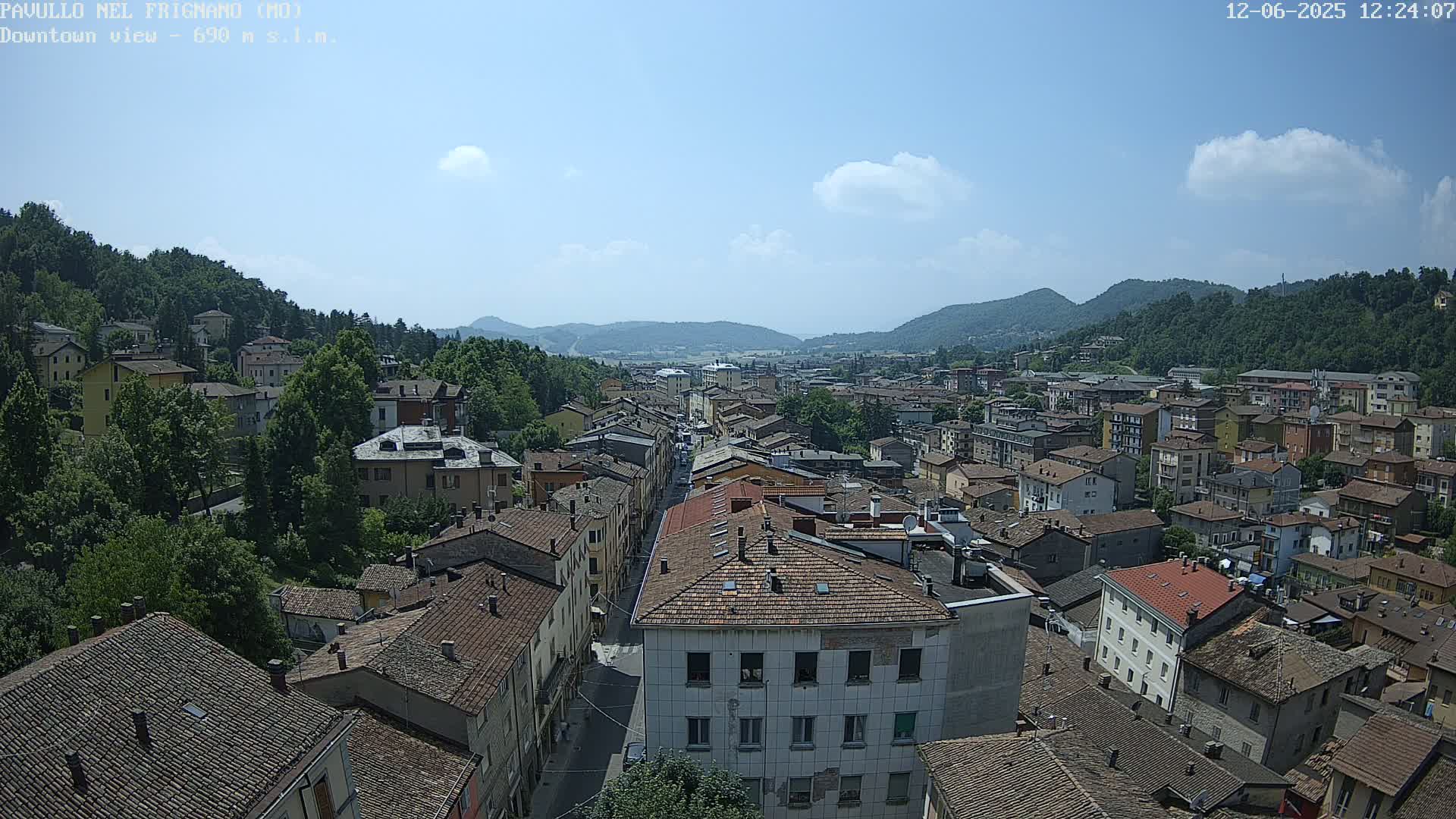 A sprawling town nestled in a valley between verdant hills under a mostly sunny sky with a few scattered clouds.