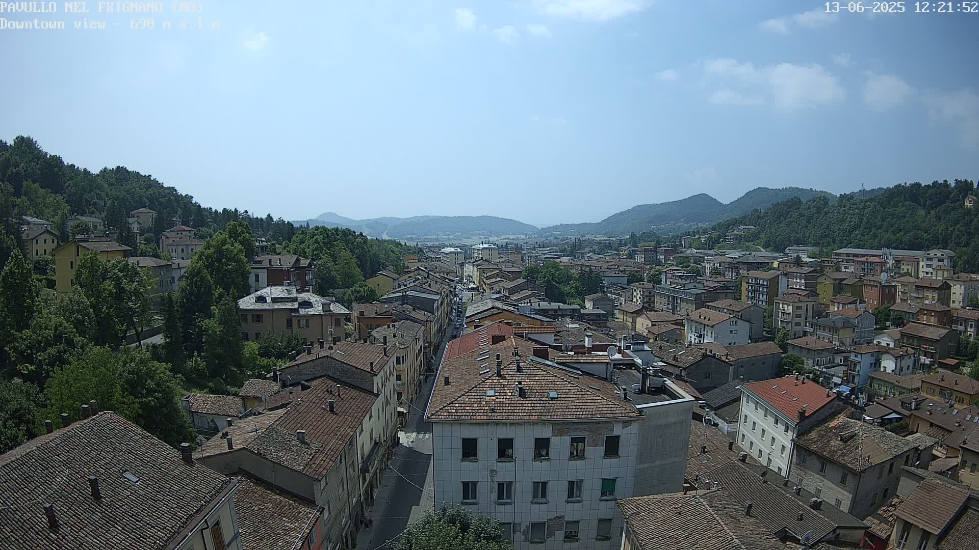 A sunlit view of a town nestled in a valley between mountains, showing numerous buildings with red tile roofs.