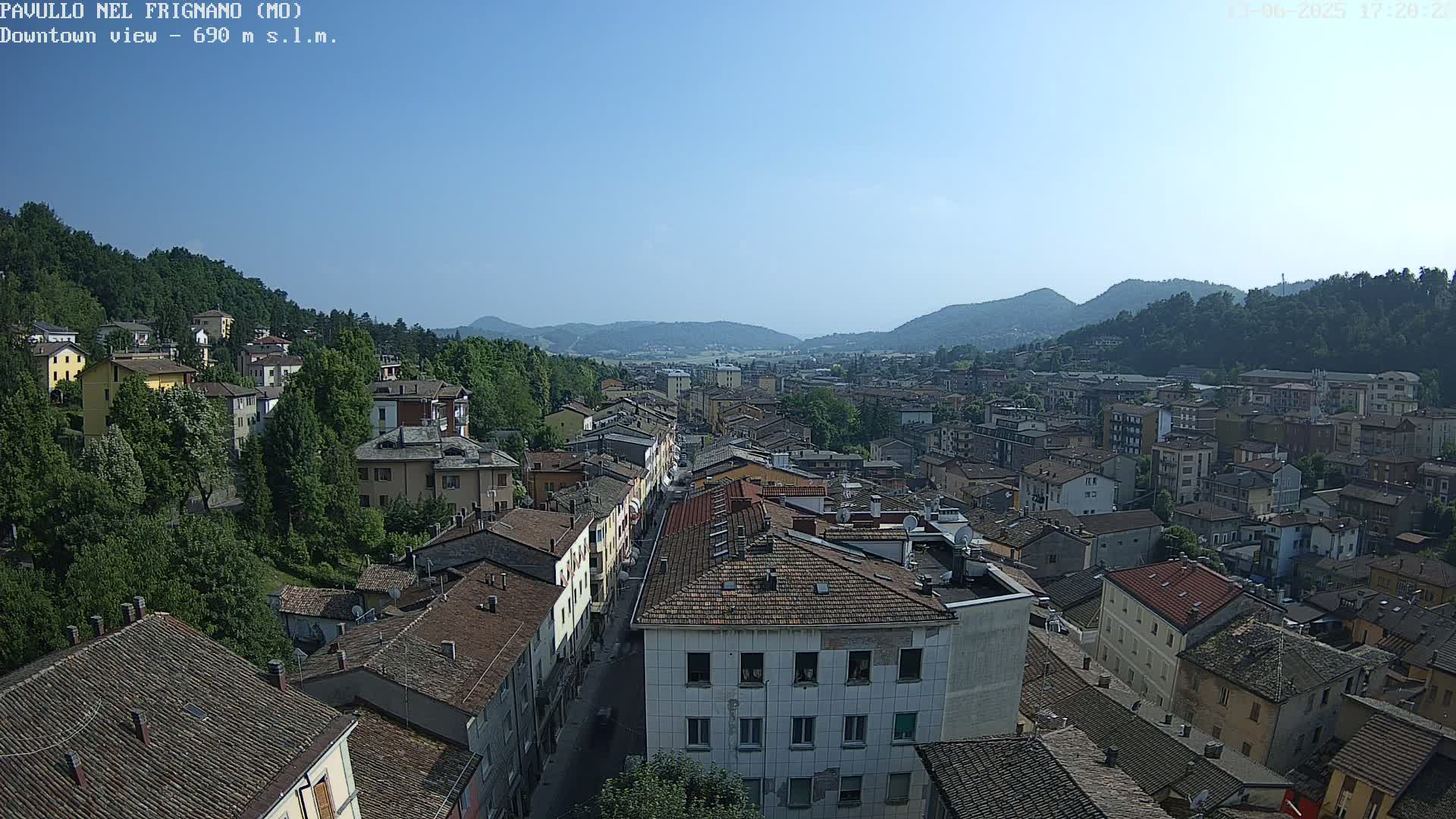 A clear, sunny day overlooks a sprawling town nestled in a valley between tree-covered hills.