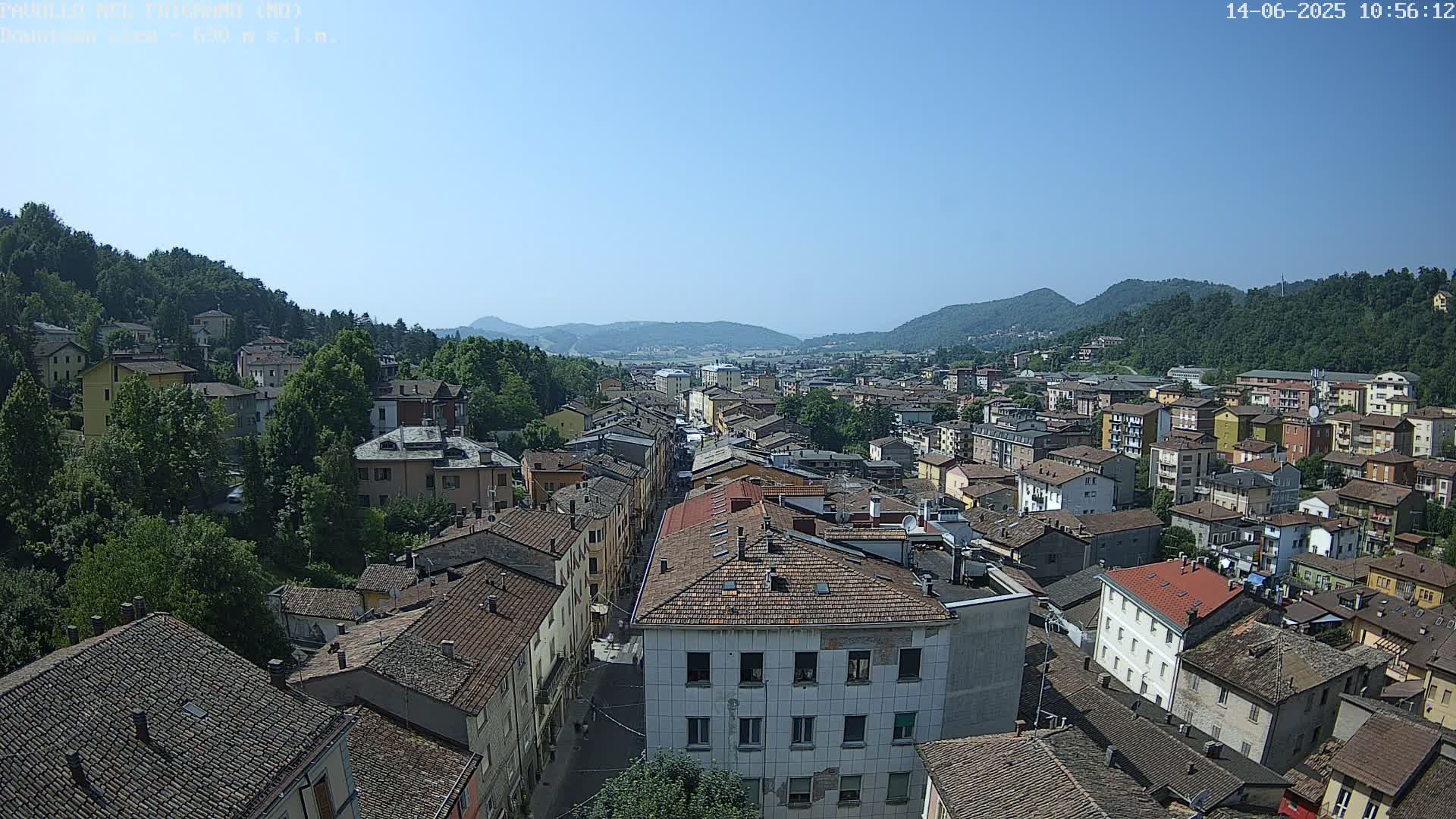 A sprawling town nestled in a valley between verdant hills under a clear, sunny sky.