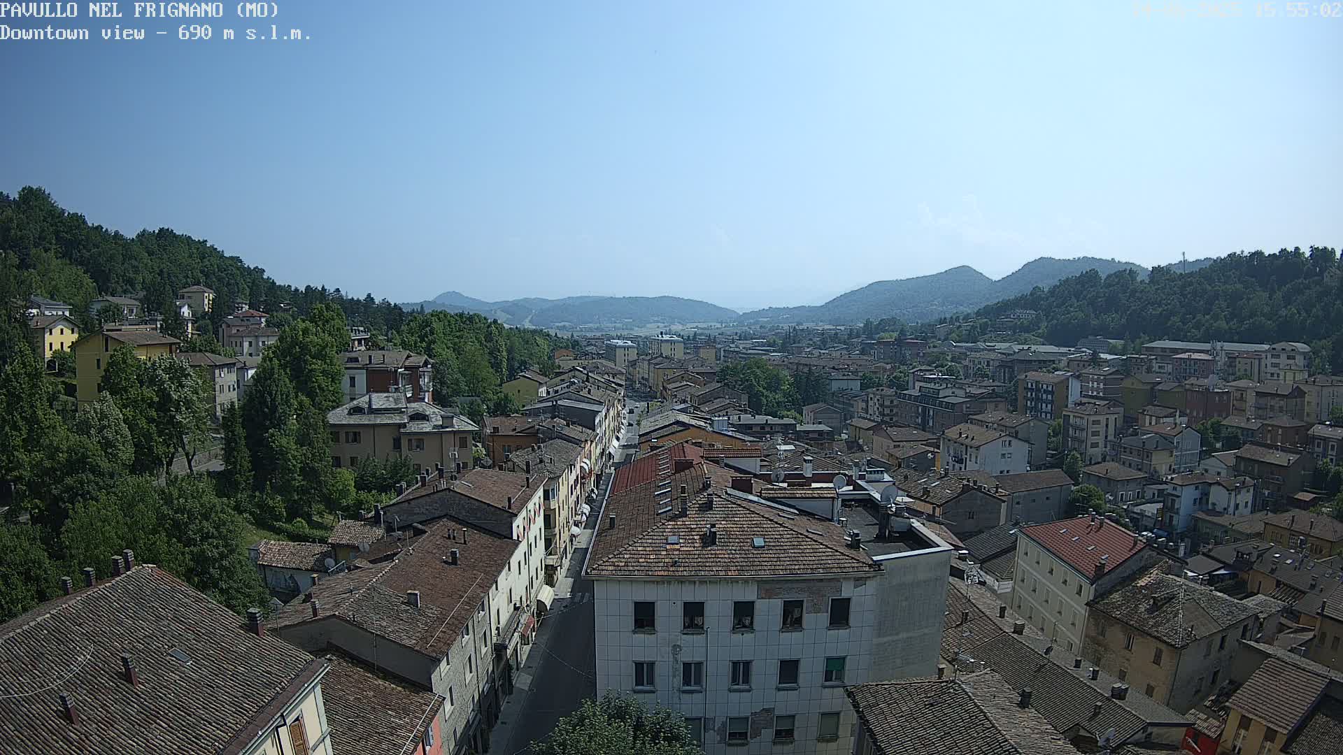 A high-angle, long shot of a town nestled in a valley on a clear, sunny day, with mountains in the background.
