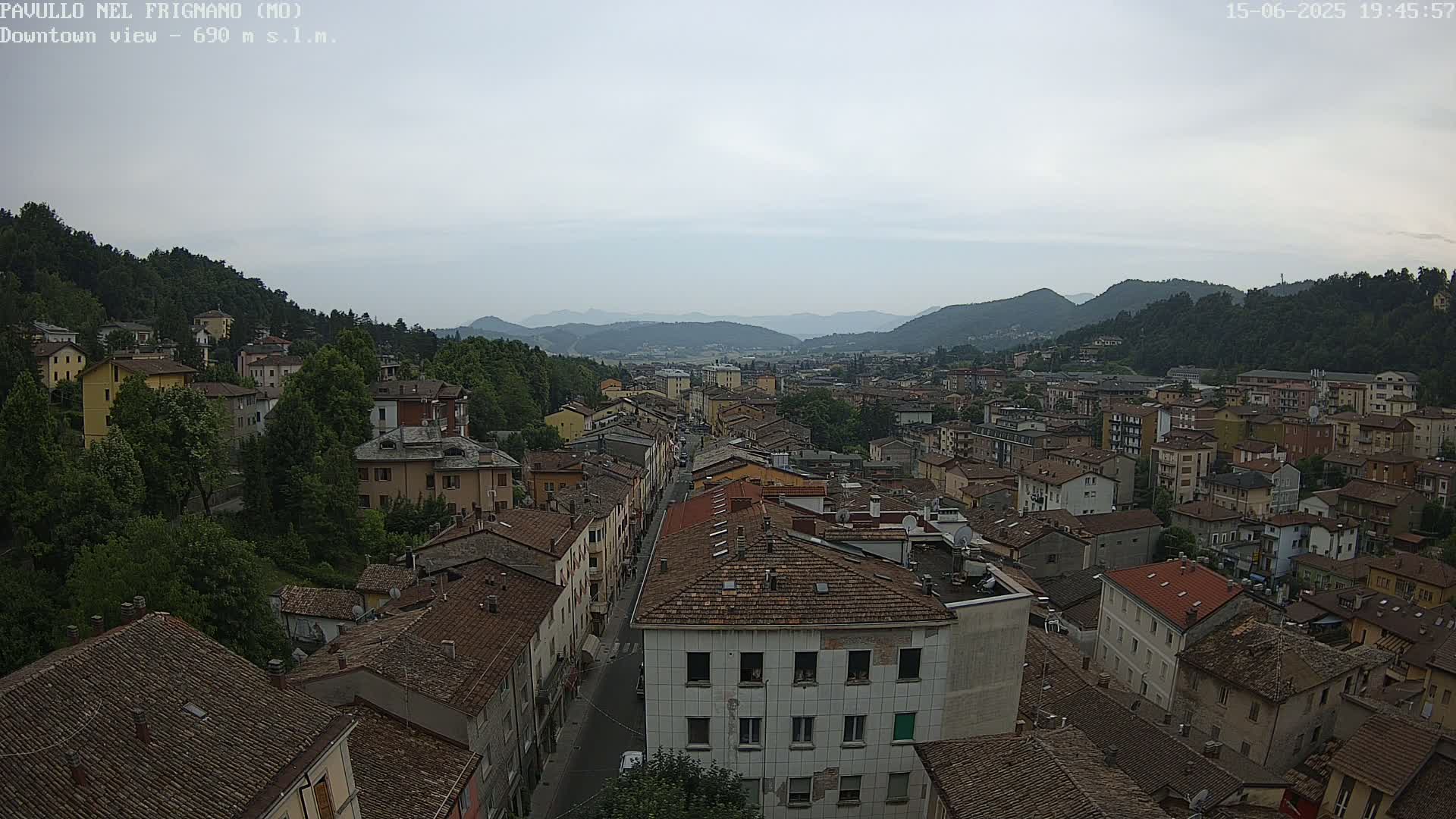 A sprawling town nestled in a valley under an overcast sky, surrounded by green hills and mountains.