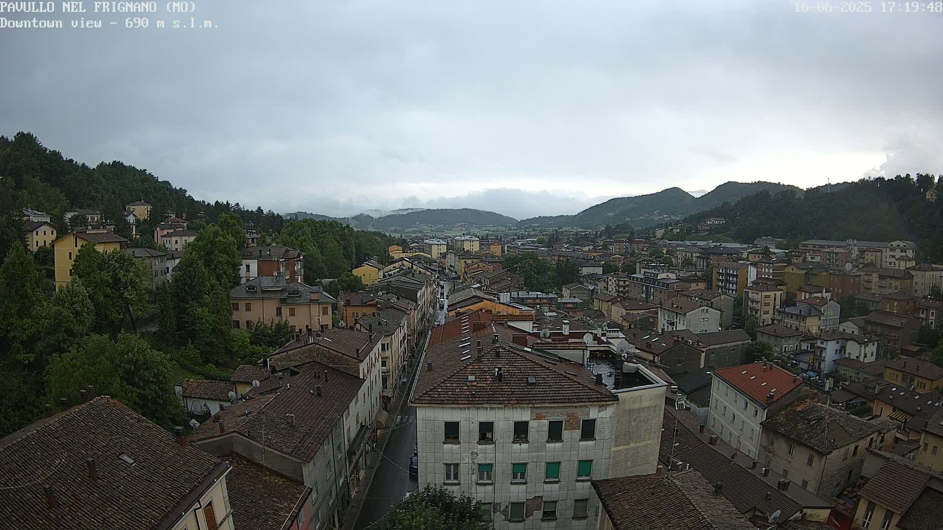 An overcast day reveals a sprawling town nestled in a valley, surrounded by verdant hills and mountains.