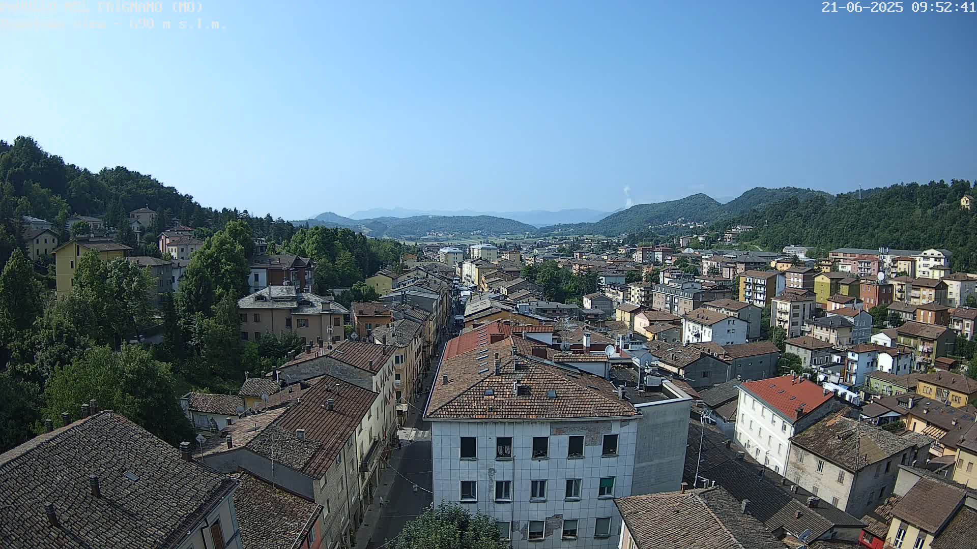 A sprawling town nestled in a valley between green hills under a clear blue sky.