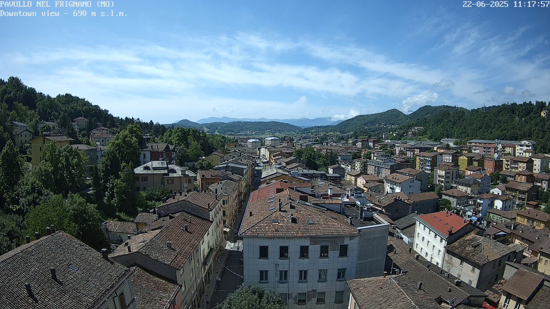 A sprawling town nestled in a valley between verdant hills under a mostly sunny sky with a few scattered clouds.