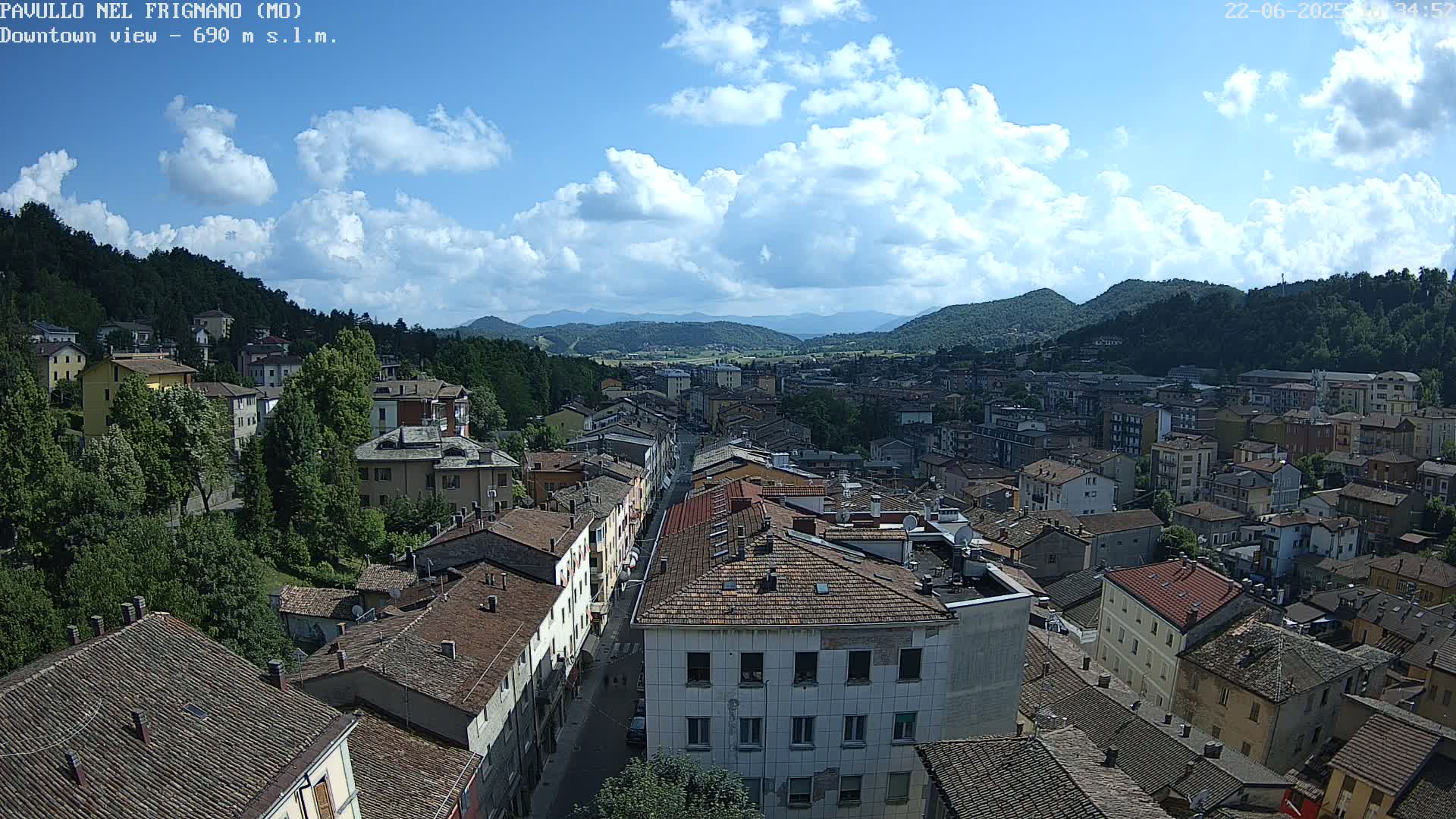 A partly cloudy daytime view of a town nestled in a valley, surrounded by green hills and mountains.